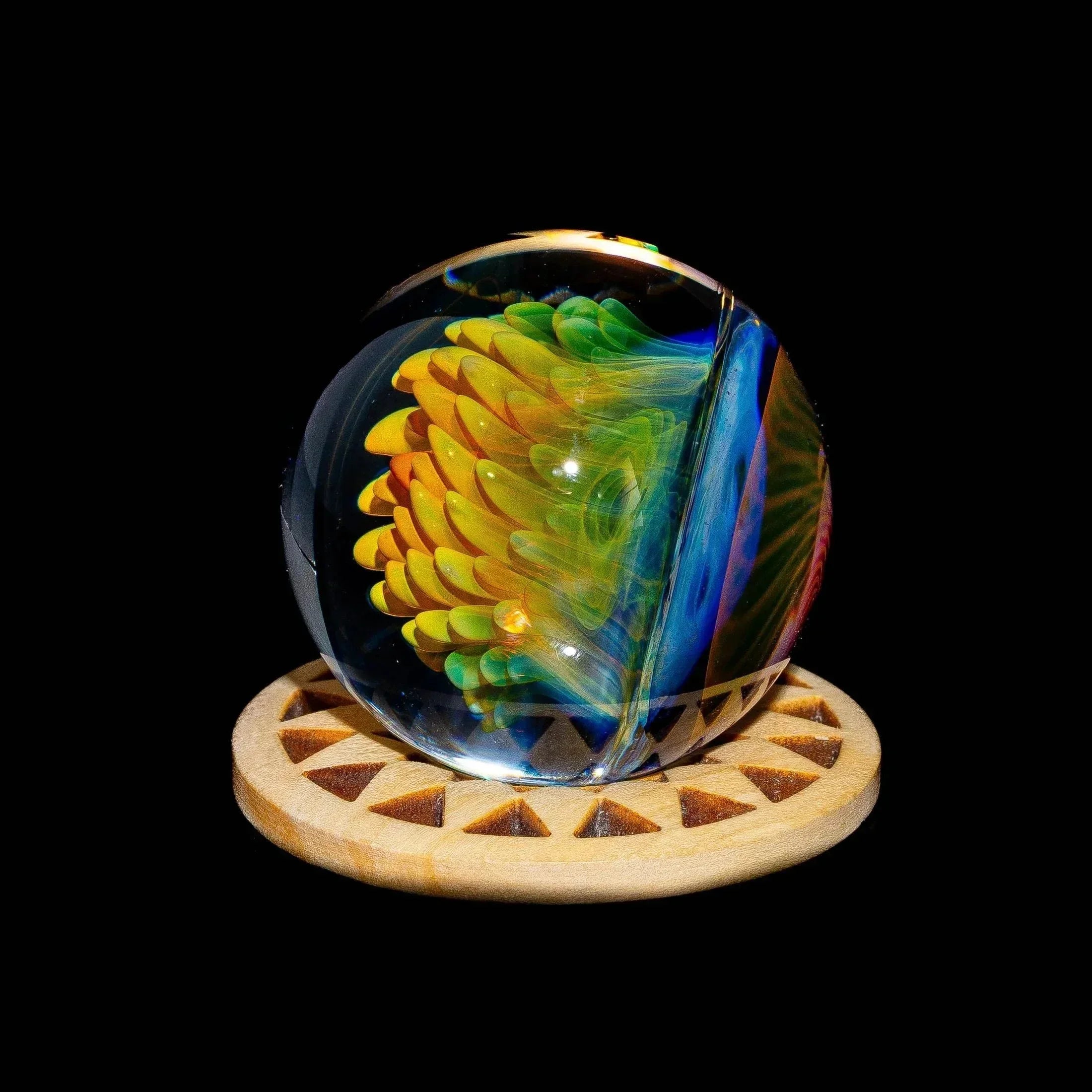 Colorful glass art marble with intricate yellow and green design, displayed on a wooden stand.