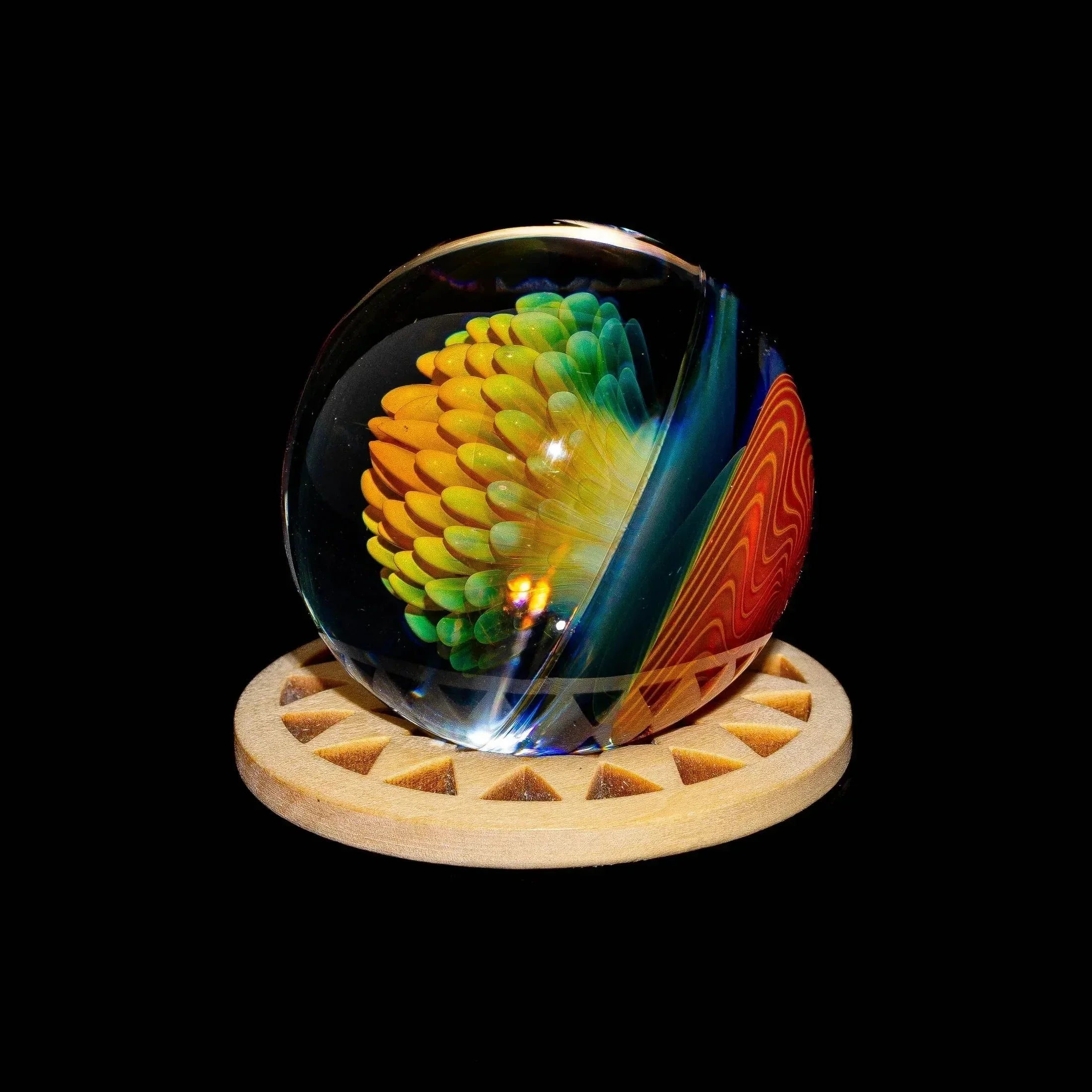 Colorful glass marble with gold pinwheel implosion design on a wooden stand, black background.