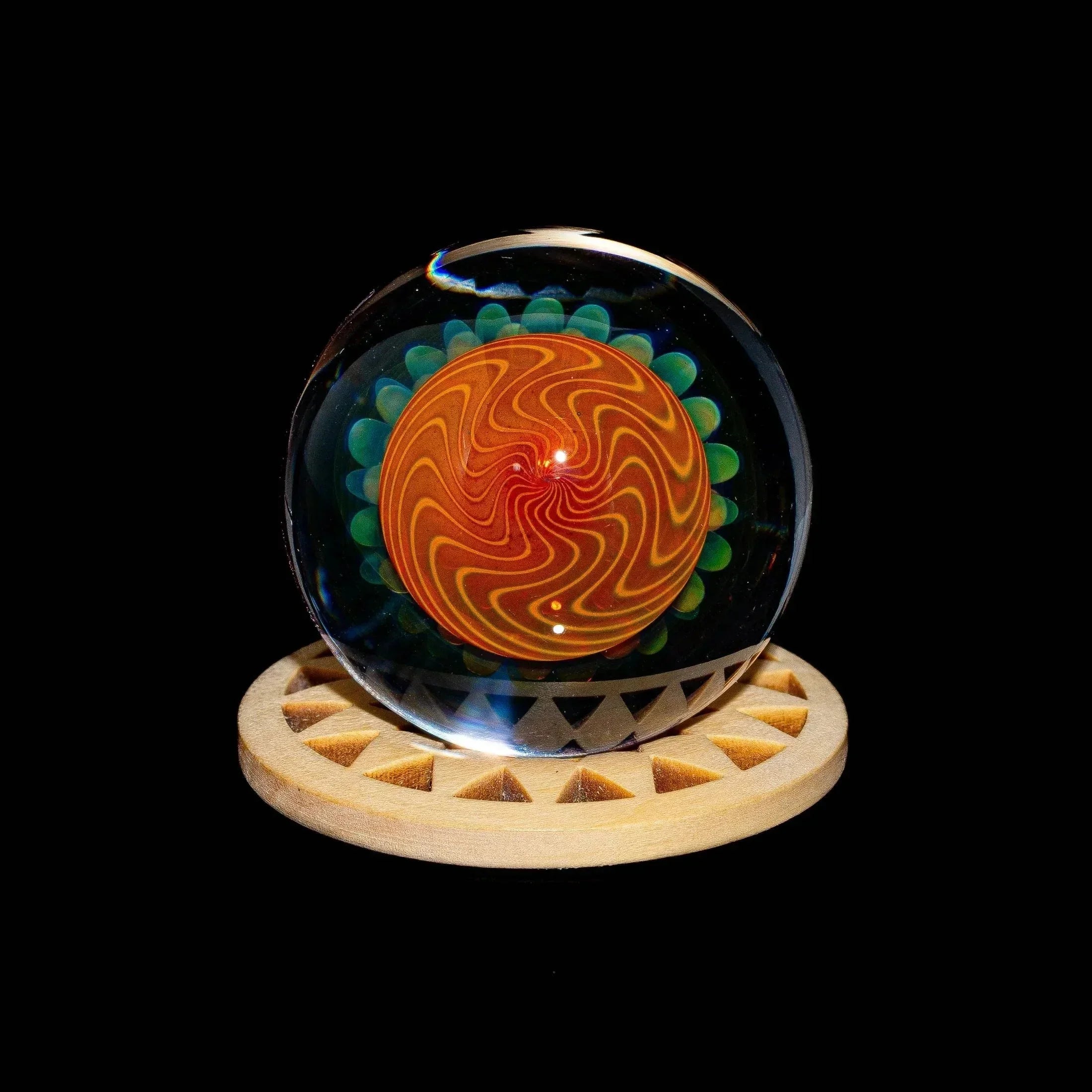 Hand-blown glass marble with gold pinwheel implosion design on a wooden stand