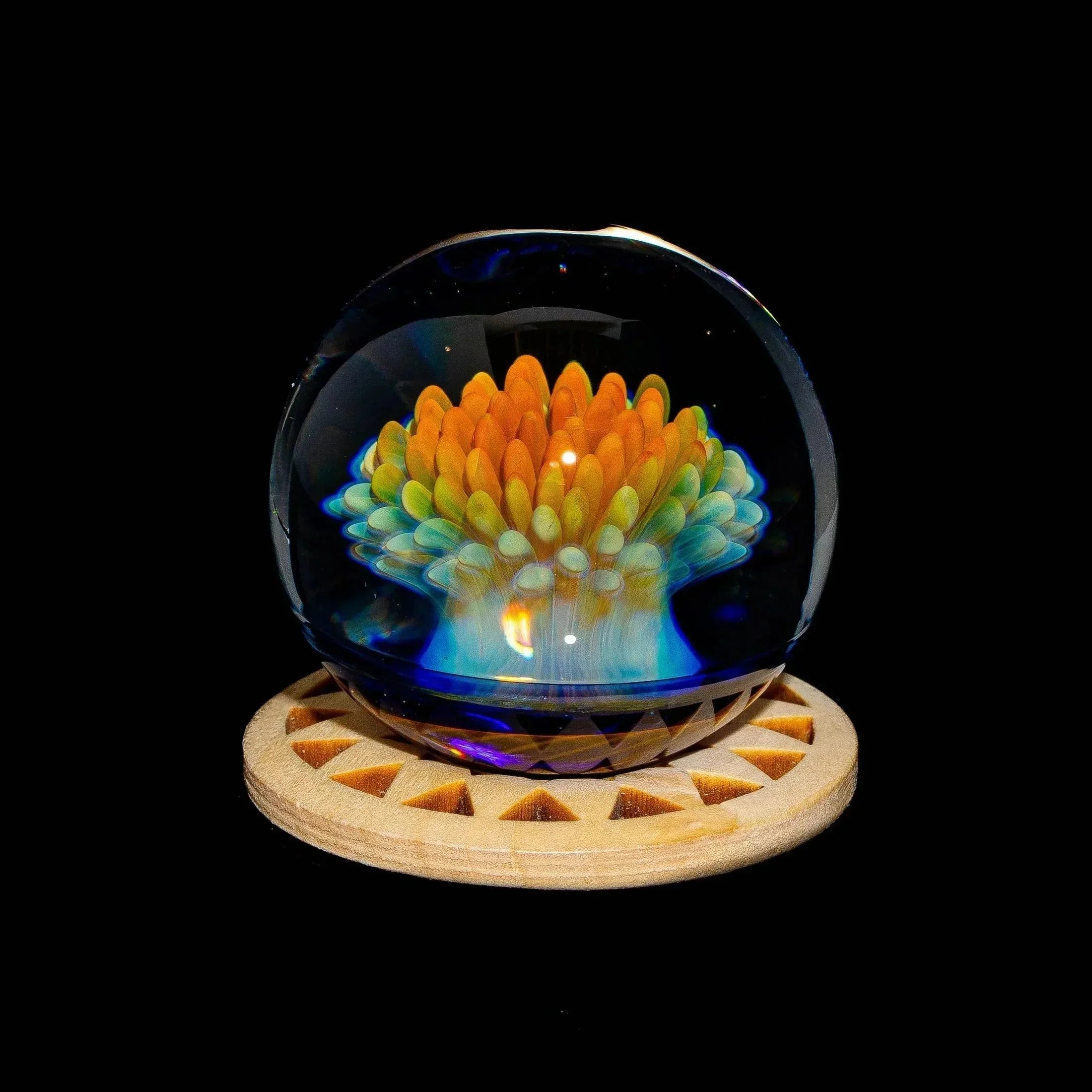 Handcrafted glass marble with vibrant flame-like implosion design on a wooden stand