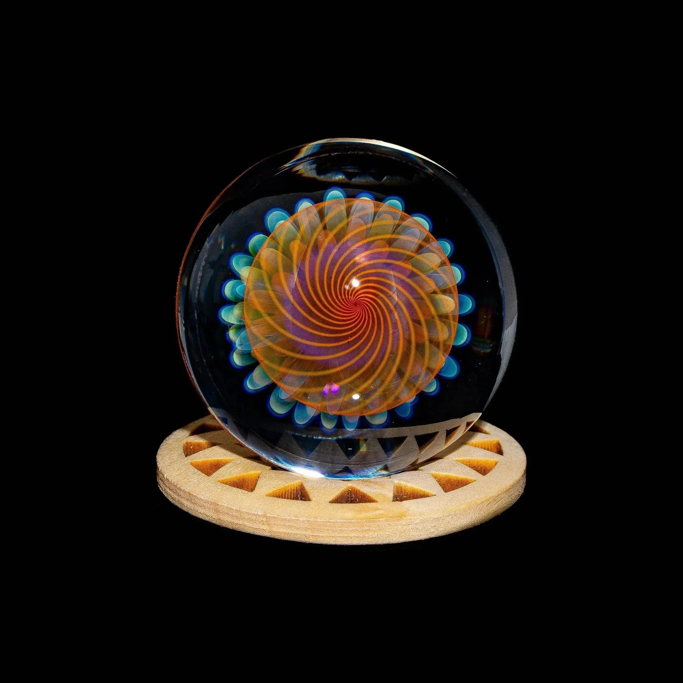 Handcrafted glass marble with spiral implosion design and blue accents on wooden stand