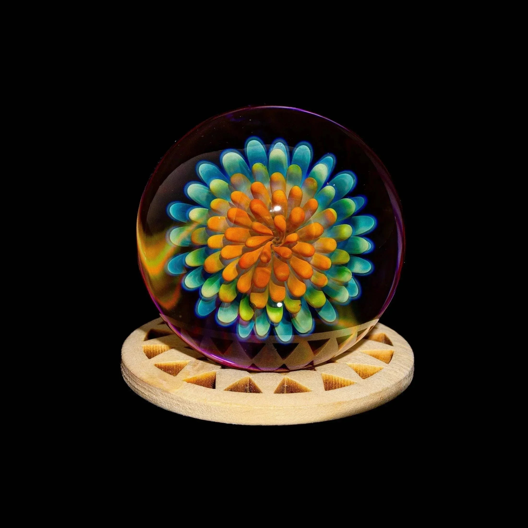 Colorful glass art marble with intricate flower implosion design on wooden stand