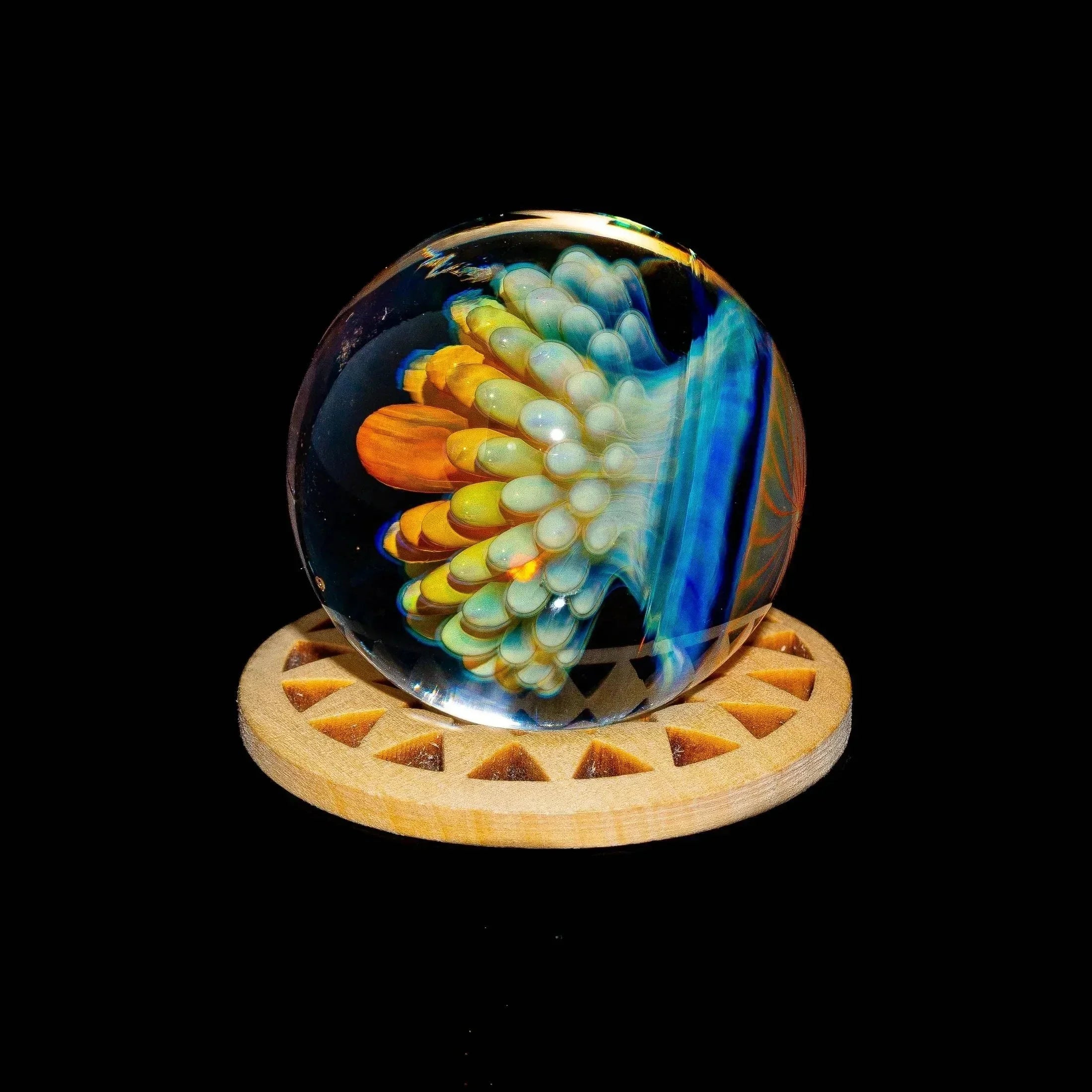 Colorful glass marble with atomic implosion design displayed on a wooden stand