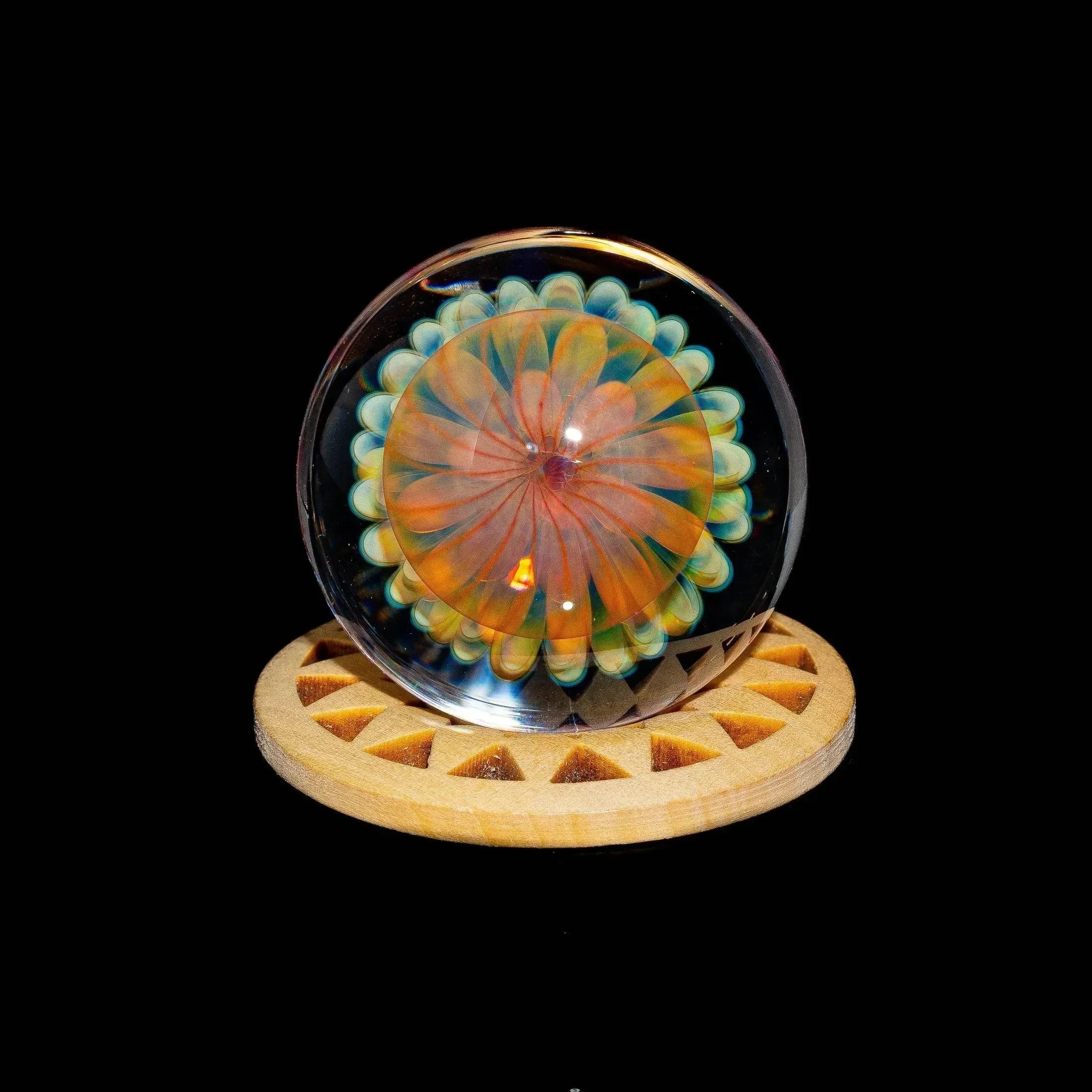 Colorful glass marble with atomic pinwheel design on a wooden stand against black background