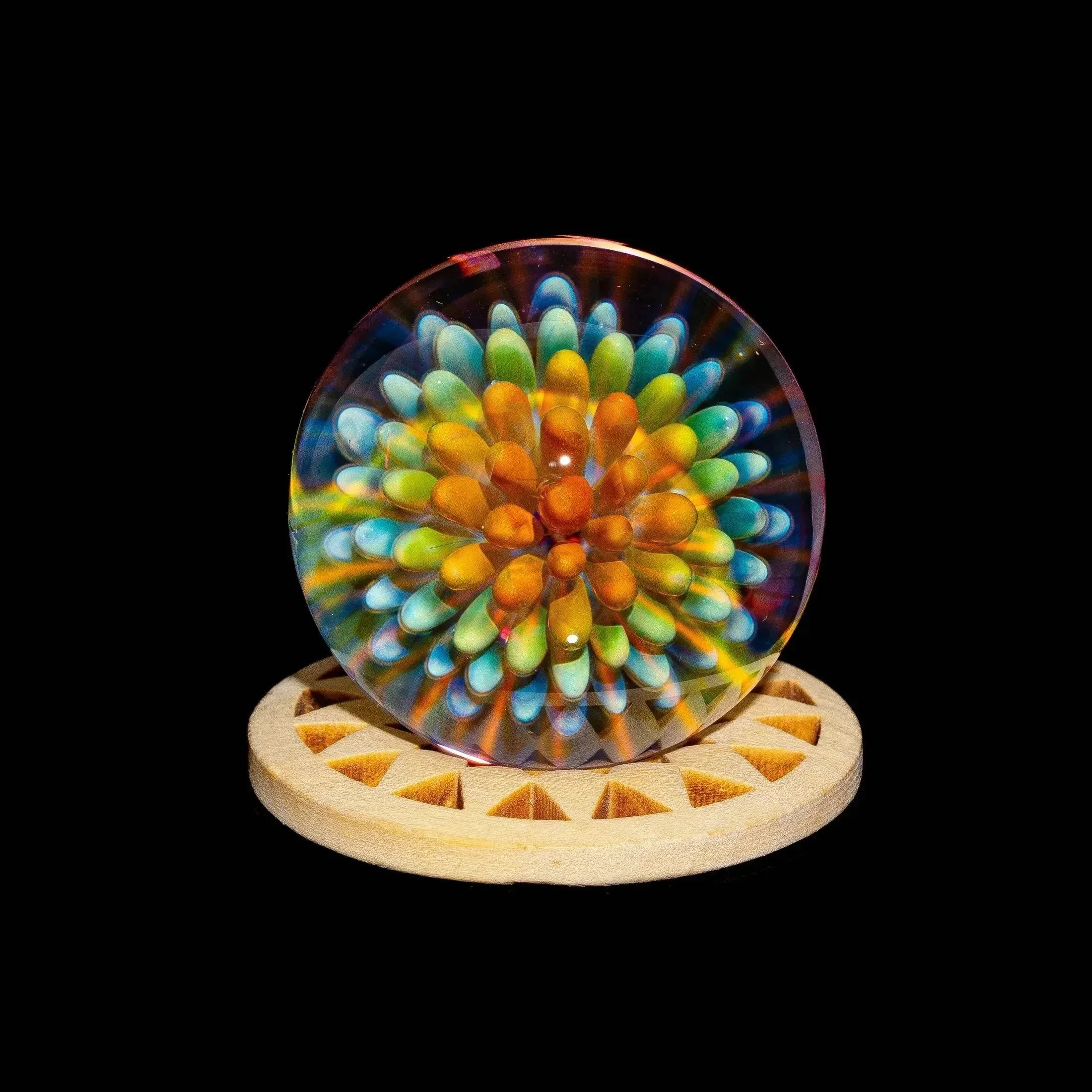 Colorful glass marble with atomic implosion pattern on a wooden stand, black background