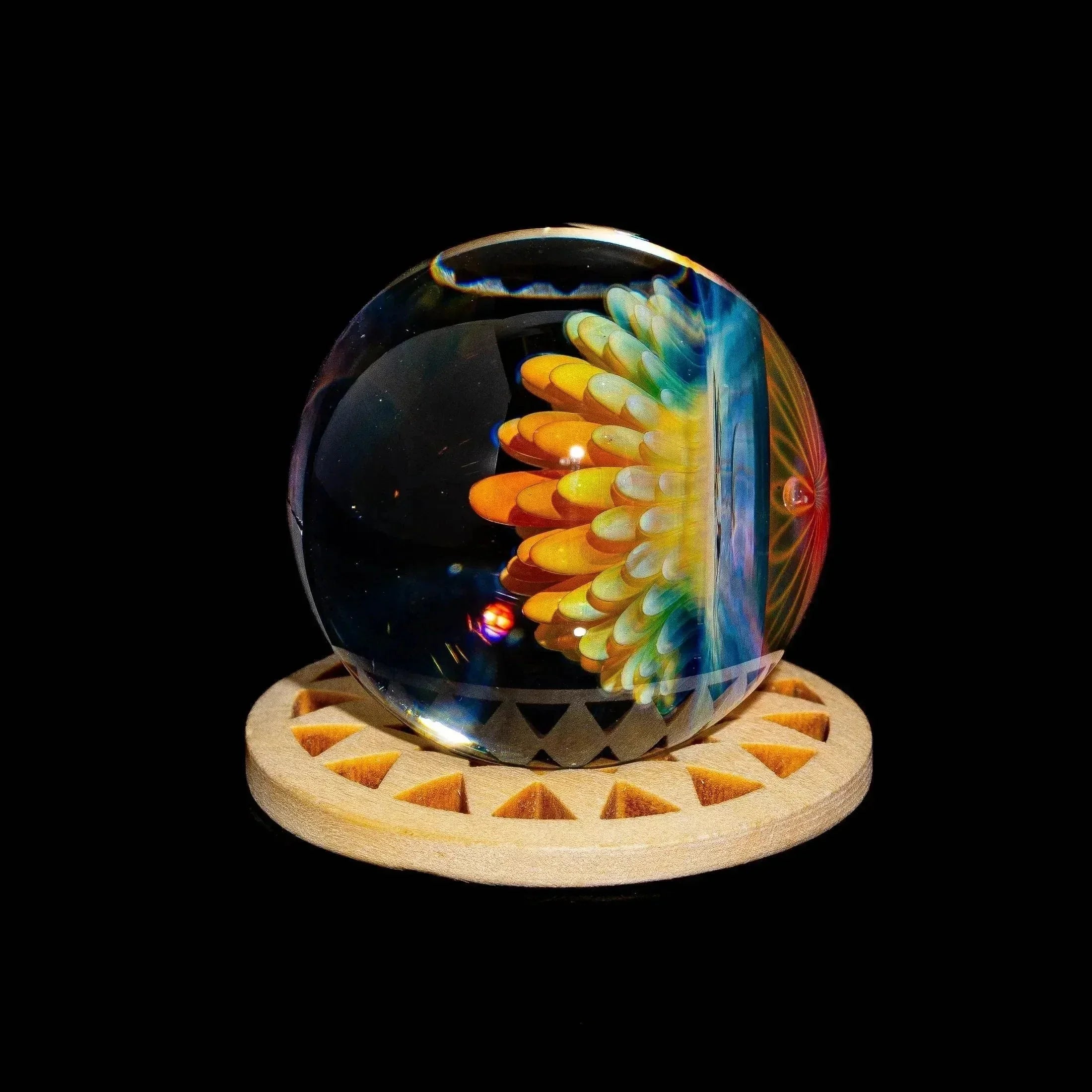Colorful glass marble with floral implosion design on wooden stand, black background.