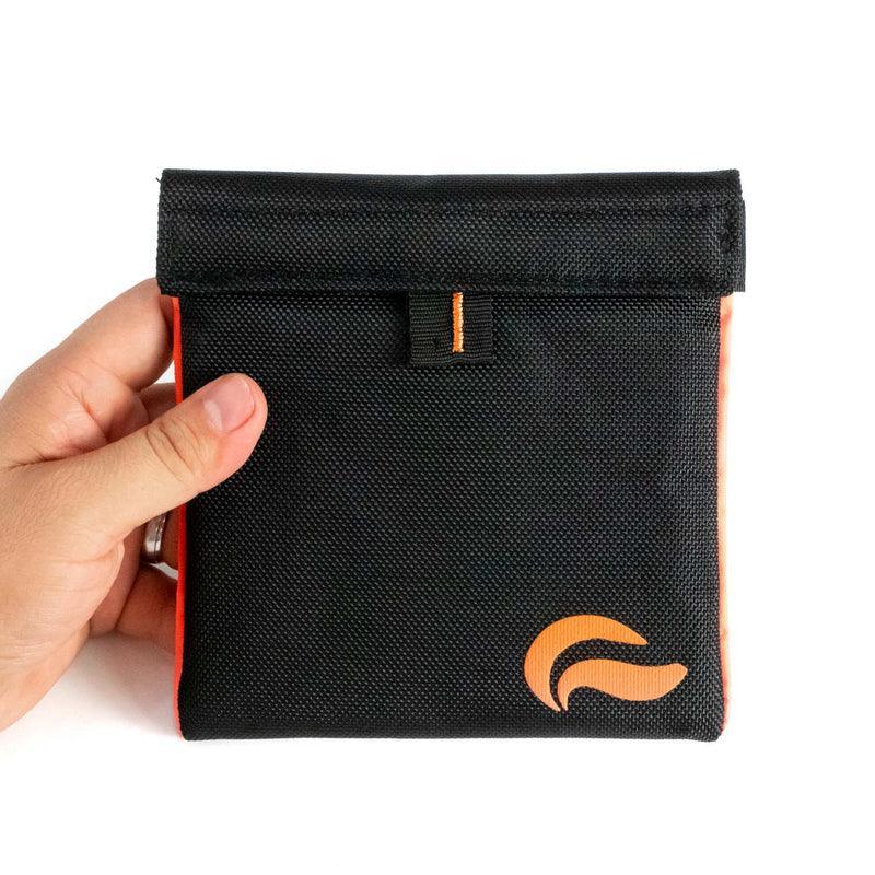 Hand holding a black smell proof pouch with orange trim and logo, odor resistant bag