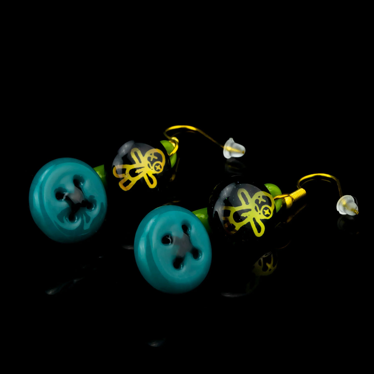 Colorful glass earrings with teal button and yellow stick figure design on black background