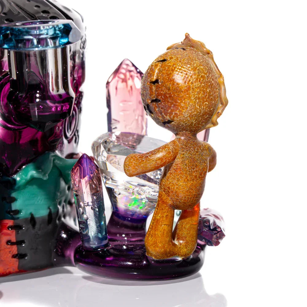 Art glass sculpture featuring colorful crystals and a textured brown figurine on white background.