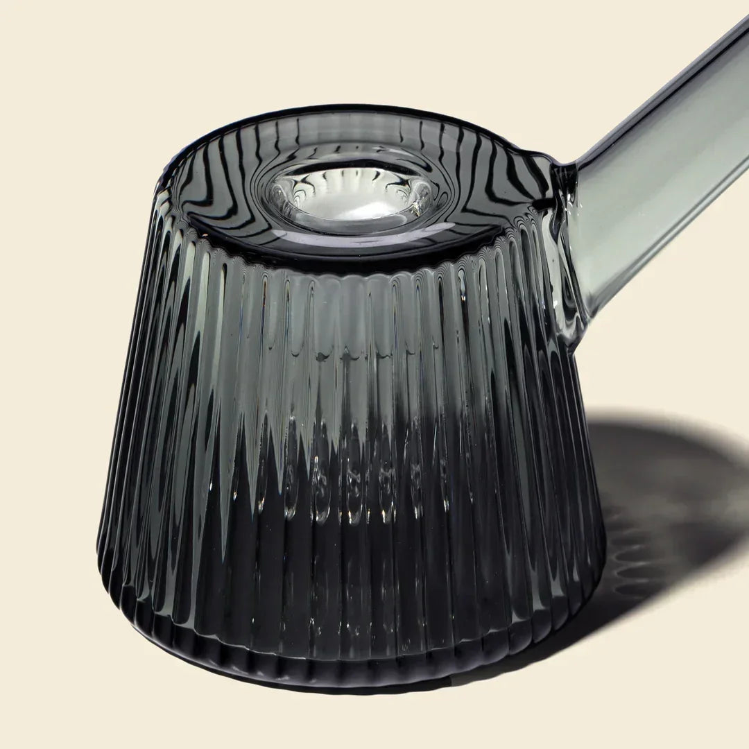 Charcoal ribbed glass bubbler with flared base and clear angled neck on beige background