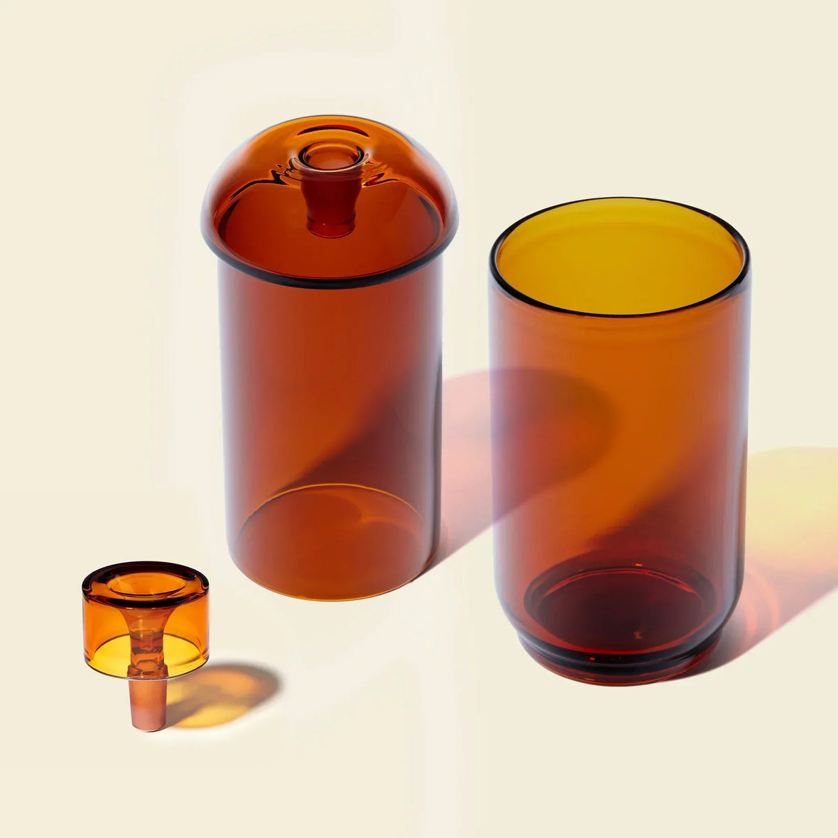 Amber glass gravity bong set with three modern, minimalist pieces on a light background