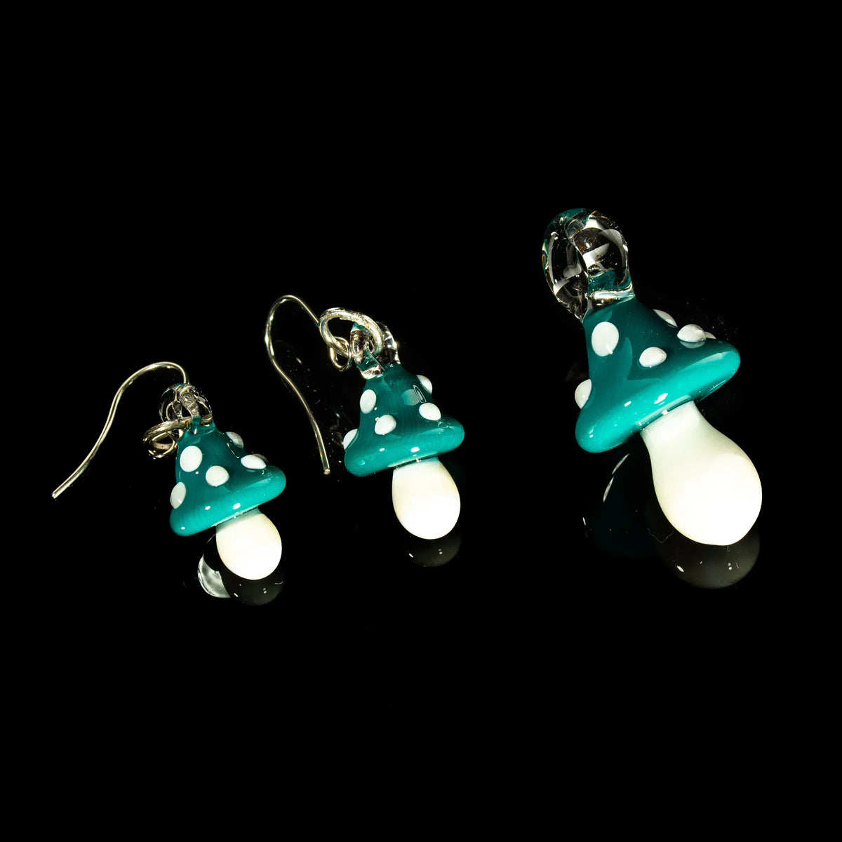 Teal glass mushroom pendant and earring set with white spots on a black background