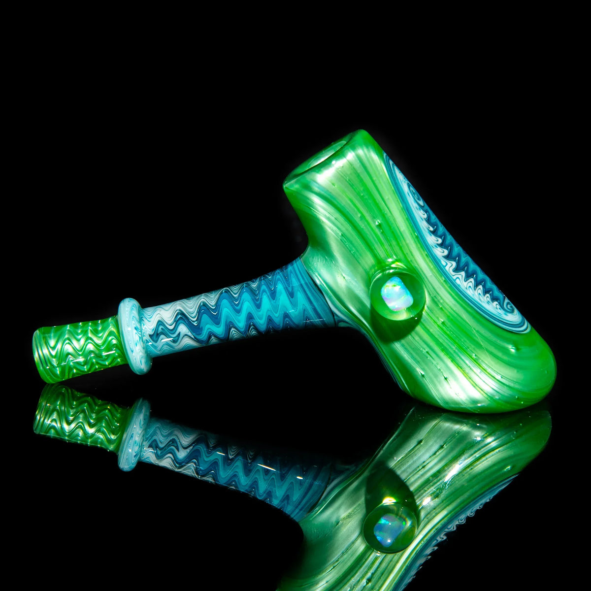 Green and blue glass hammer pipe with linework pattern on a black reflective surface