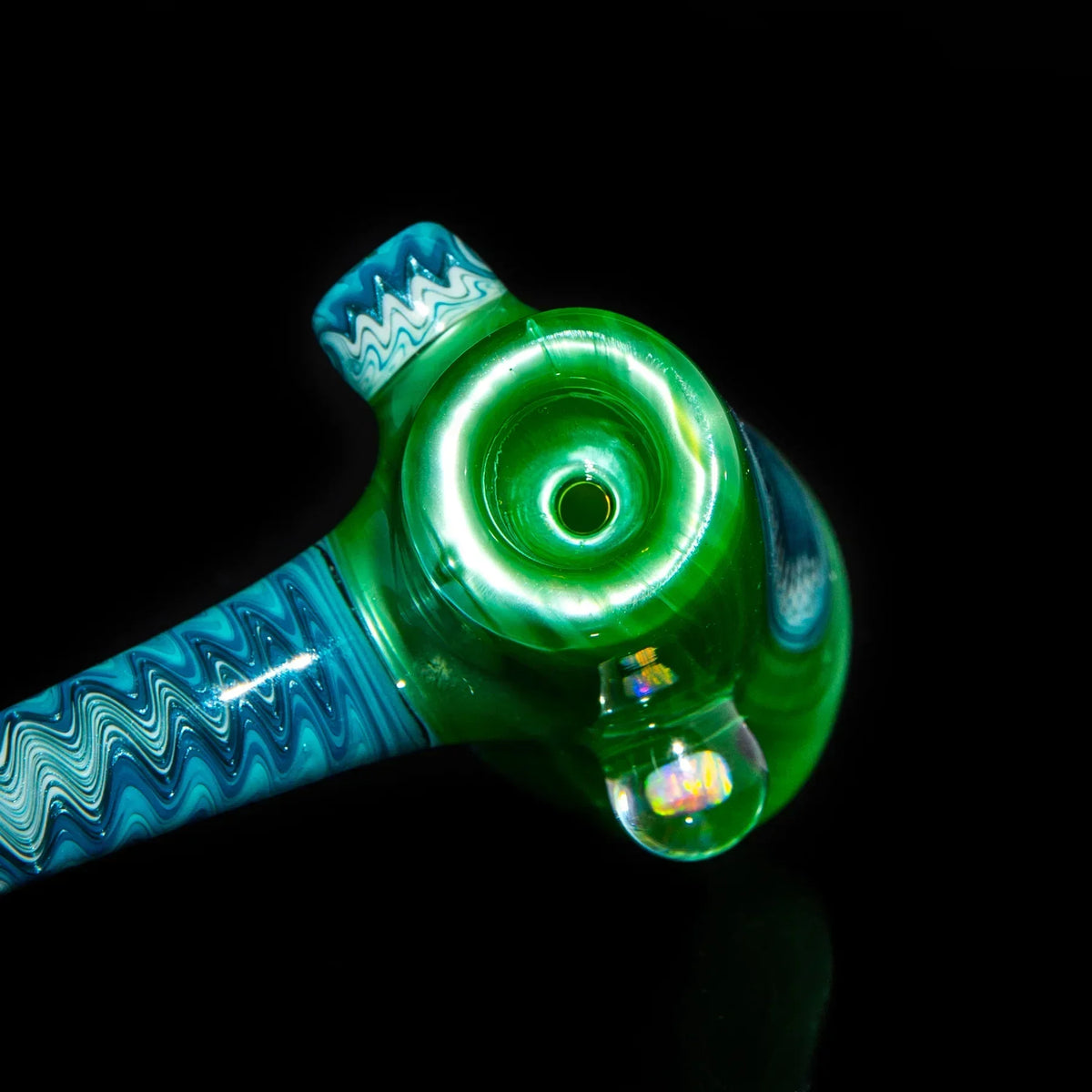 Close-up of a green and blue glass hand pipe with intricate linework design on black background.