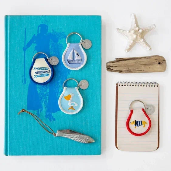 Nautical patch keychains with fish, sailboat, pelican, and dog designs on a book and notepad