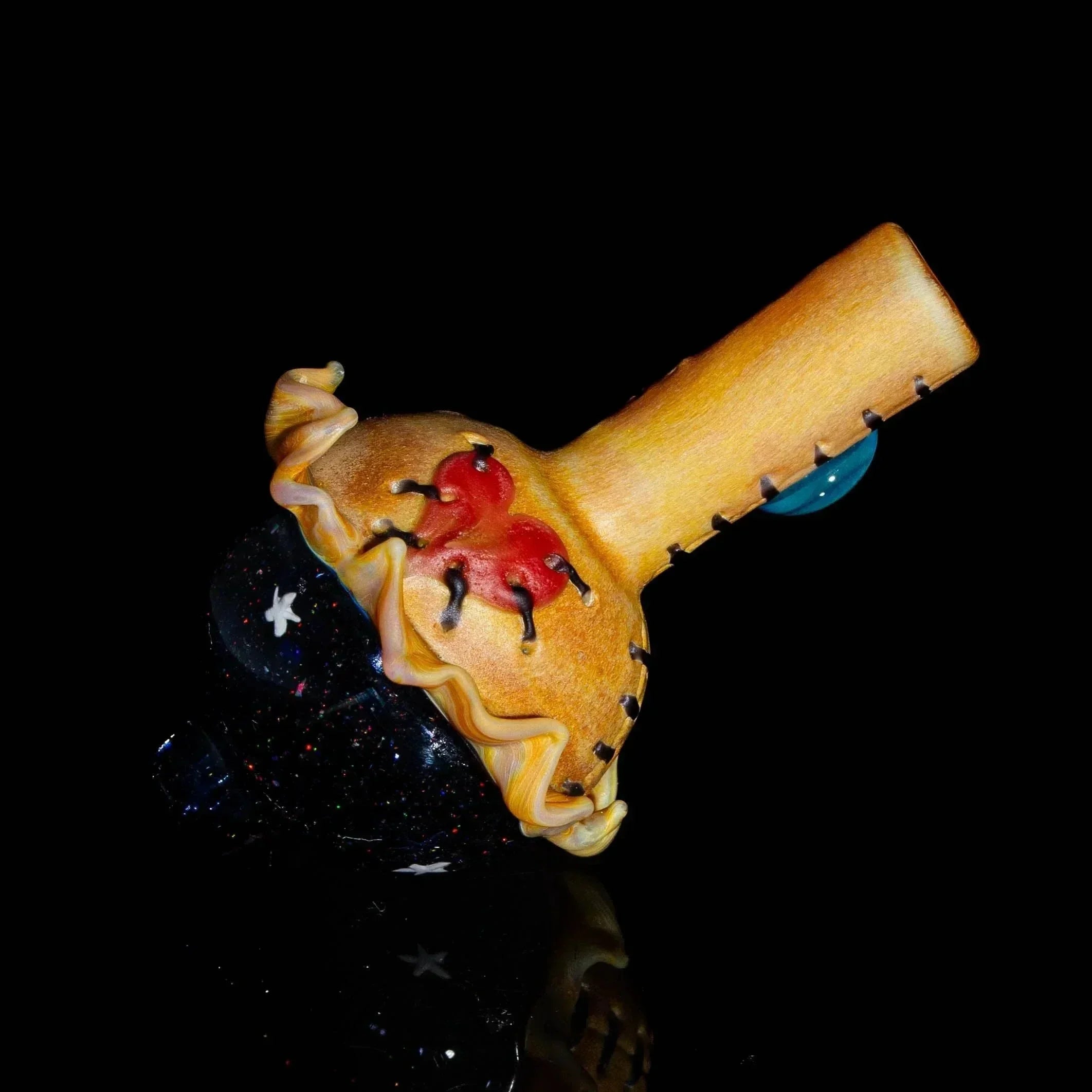 Artistic glass pipe with a colorful, stitched doll design on a black reflective background