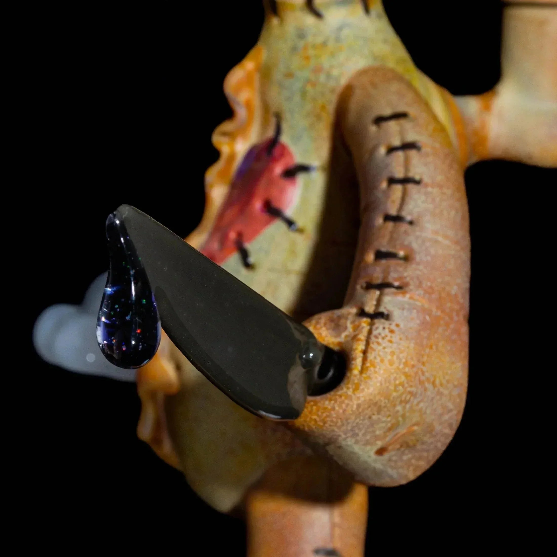 Close-up of intricate glass art sculpture featuring stitched details and a black blade element