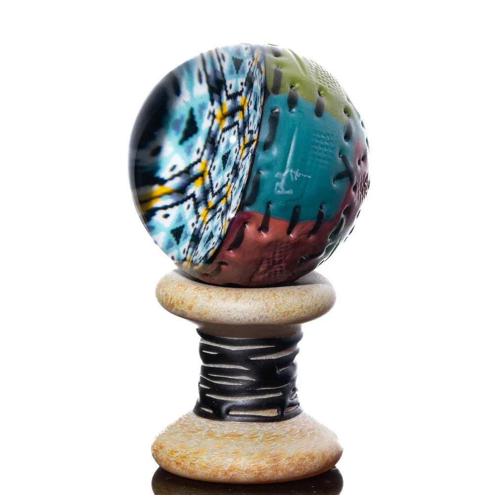 Colorful handmade glass marble with quilted texture on a spool display stand