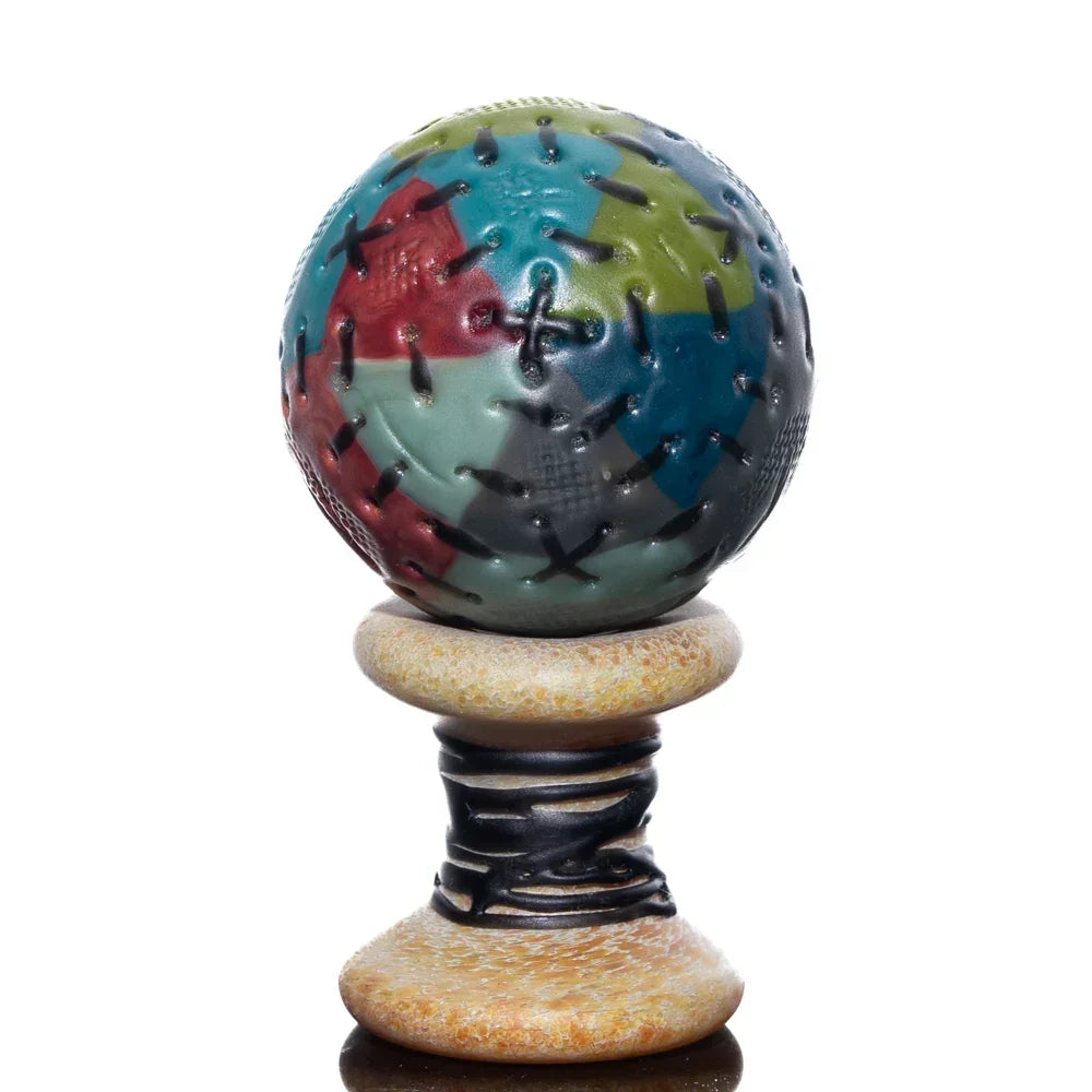 Colorful marble-patterned glass carb cap with stitched details on a decorative spool stand.