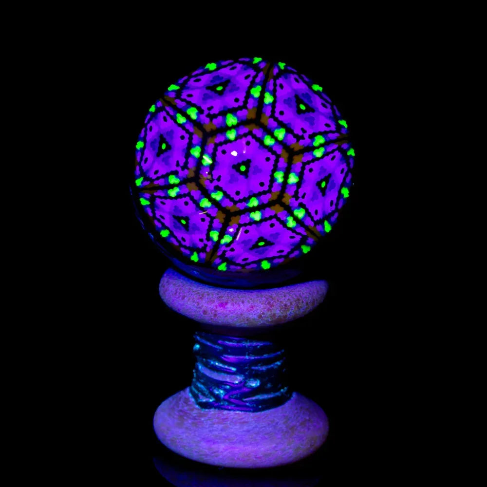 UV reactive glass marble with purple geometric patterns and green accents on spool stand