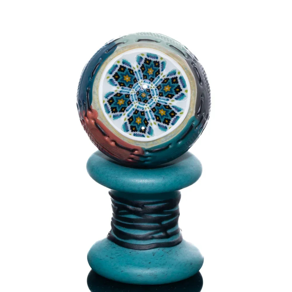 Colorful glass marble with intricate mandala pattern on a turquoise spool stand