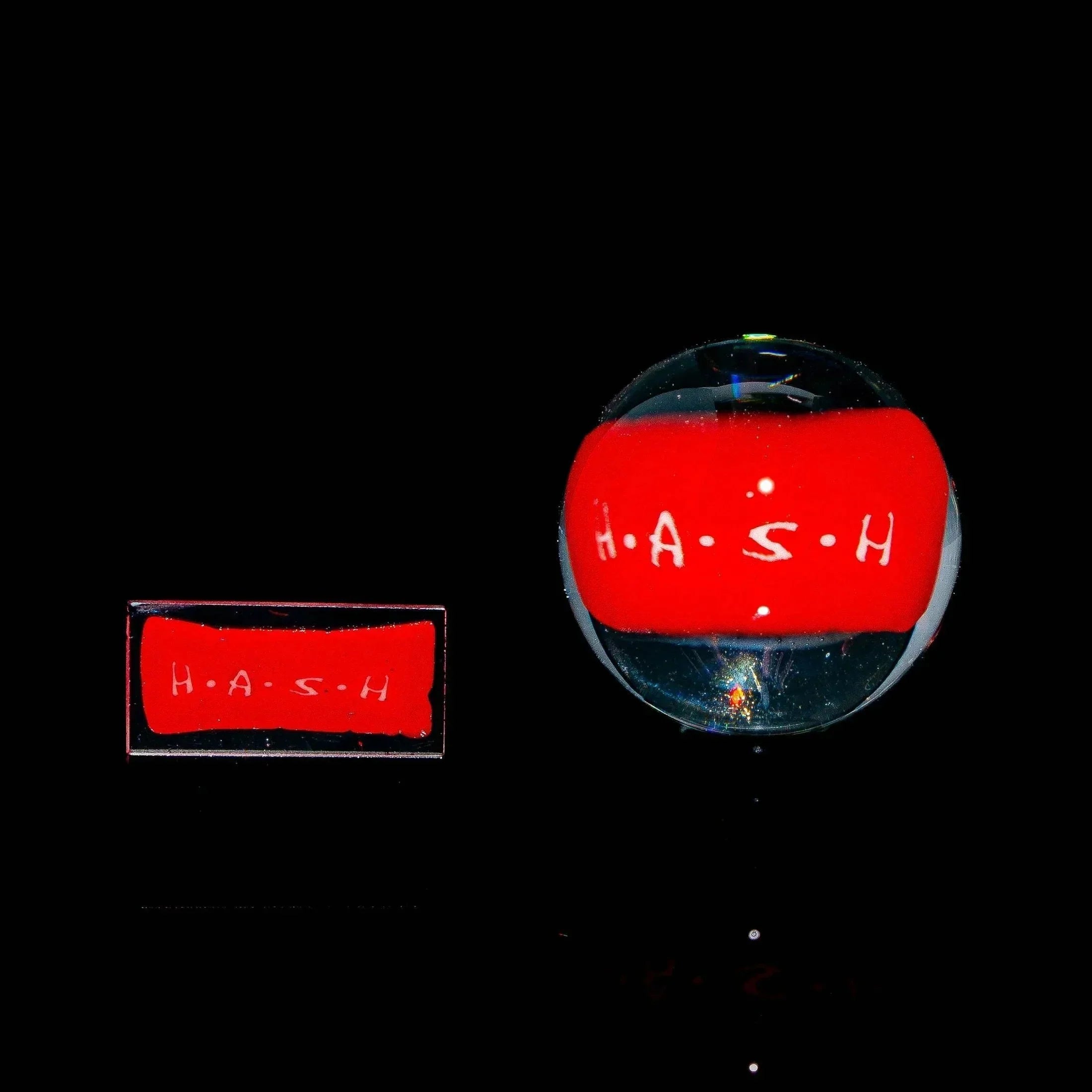Clear glass marble and chip with red center labeled H.A.S.H. on black background.