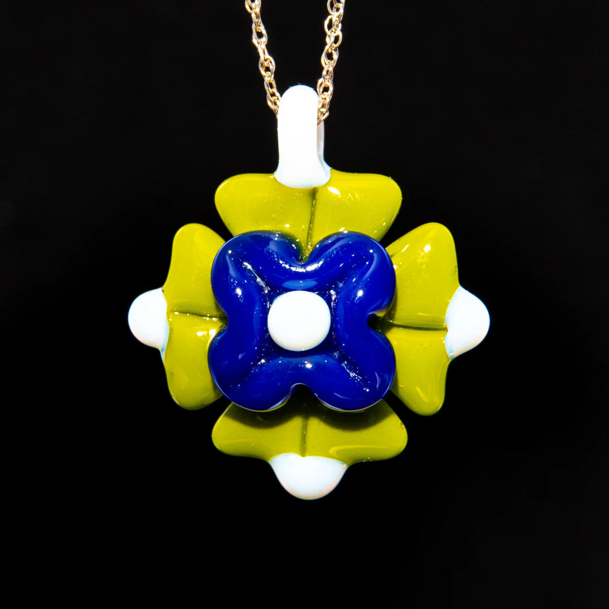 Blue and green glass pendant with floral design on gold chain, studio background