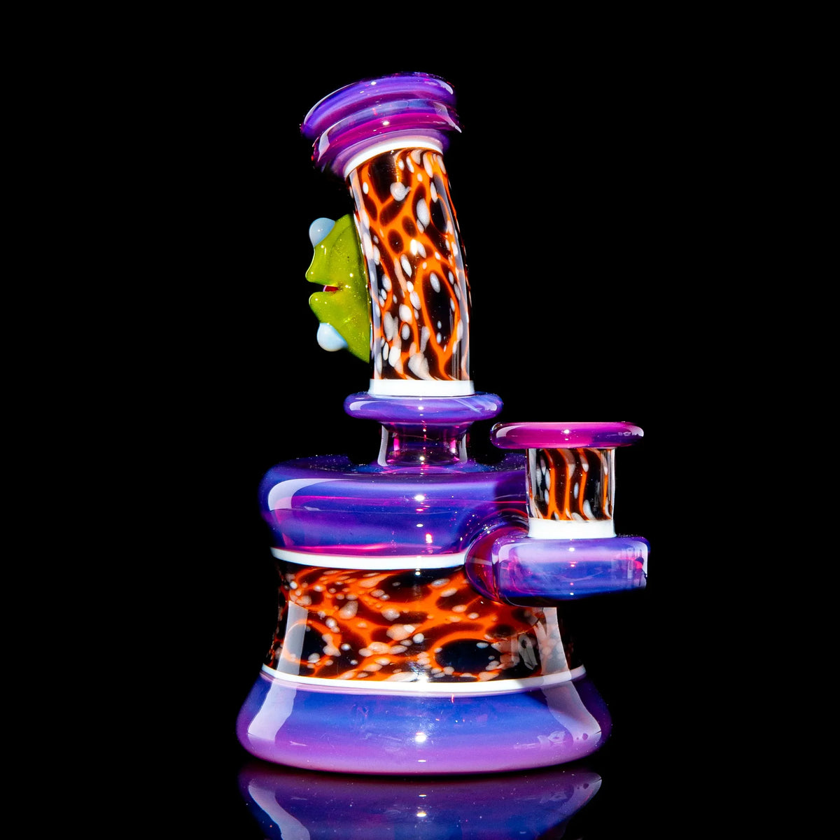 Colorful glass mini water pipe with vibrant patterns and a green frog detail on black background.