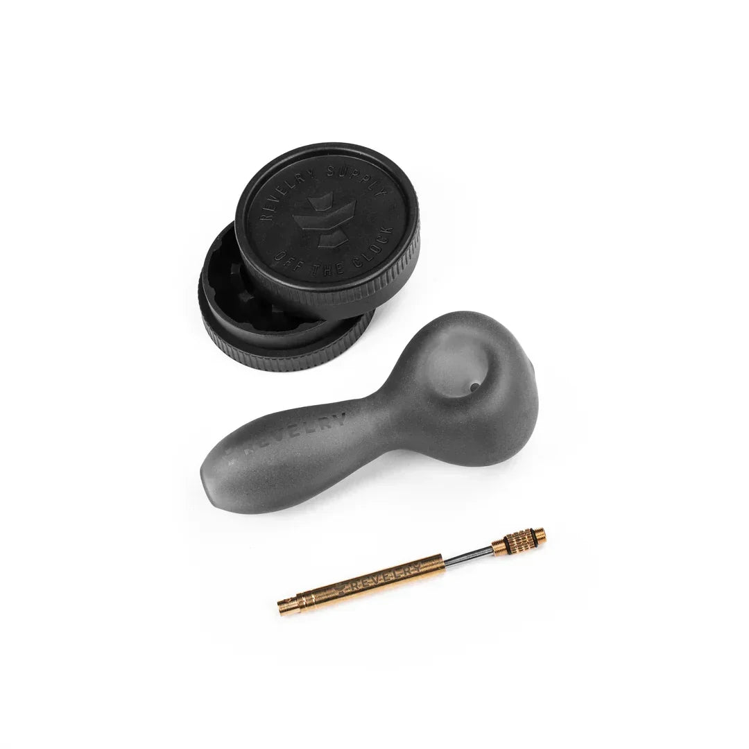 Black herb grinder, matte black glass hand pipe, and metal cleaning tool on white background.