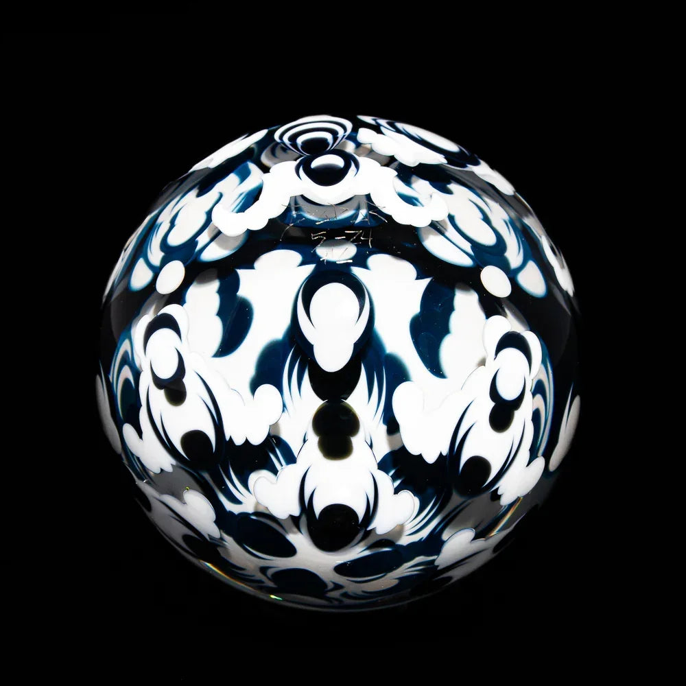 Hand-blown glass orb with intricate black and white patterns on a black background