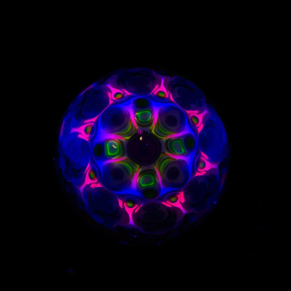 UV-reactive heady glass marble with intricate blue, pink, and green patterns on black