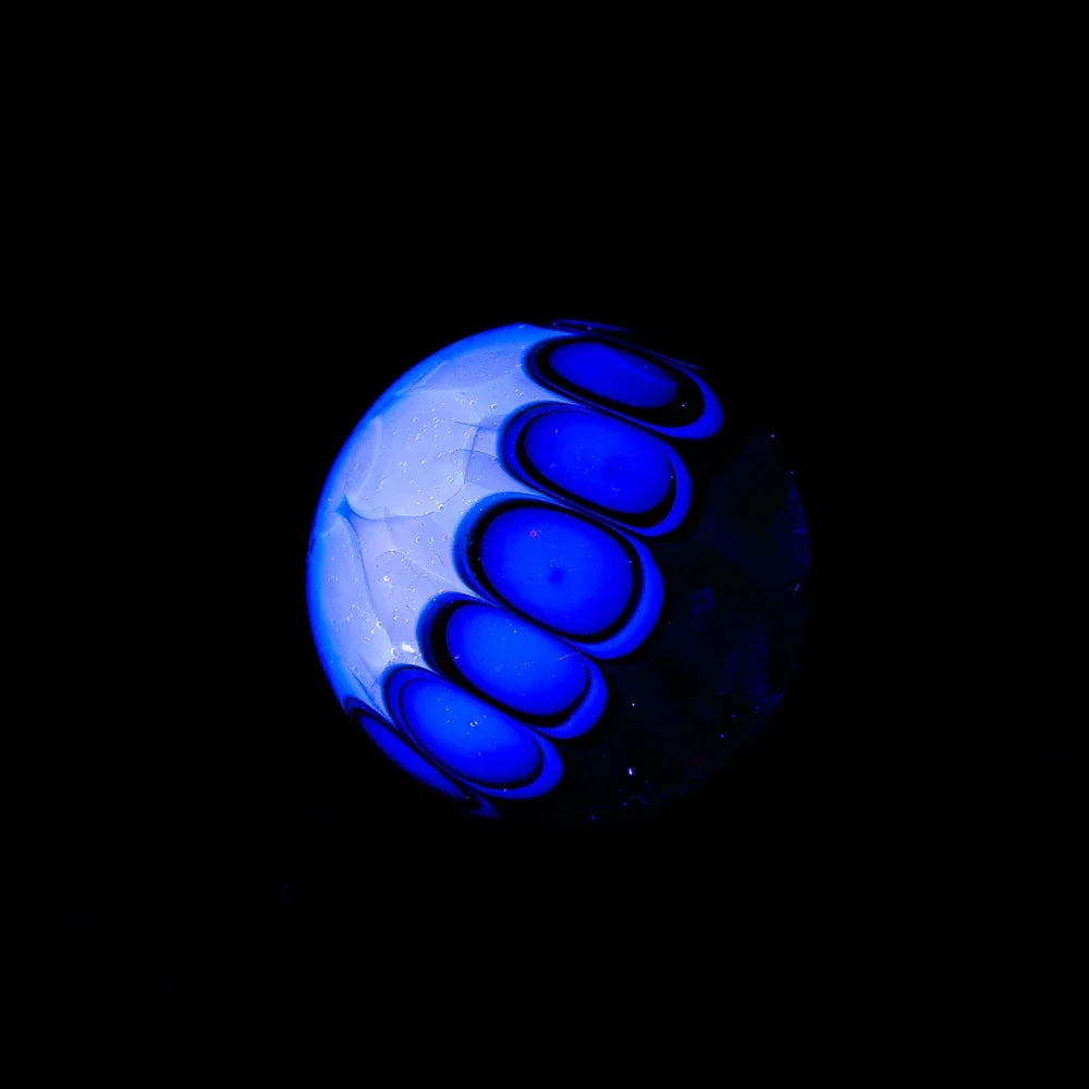 Handcrafted glass marble with silver fume and blue stardust accents on black background.