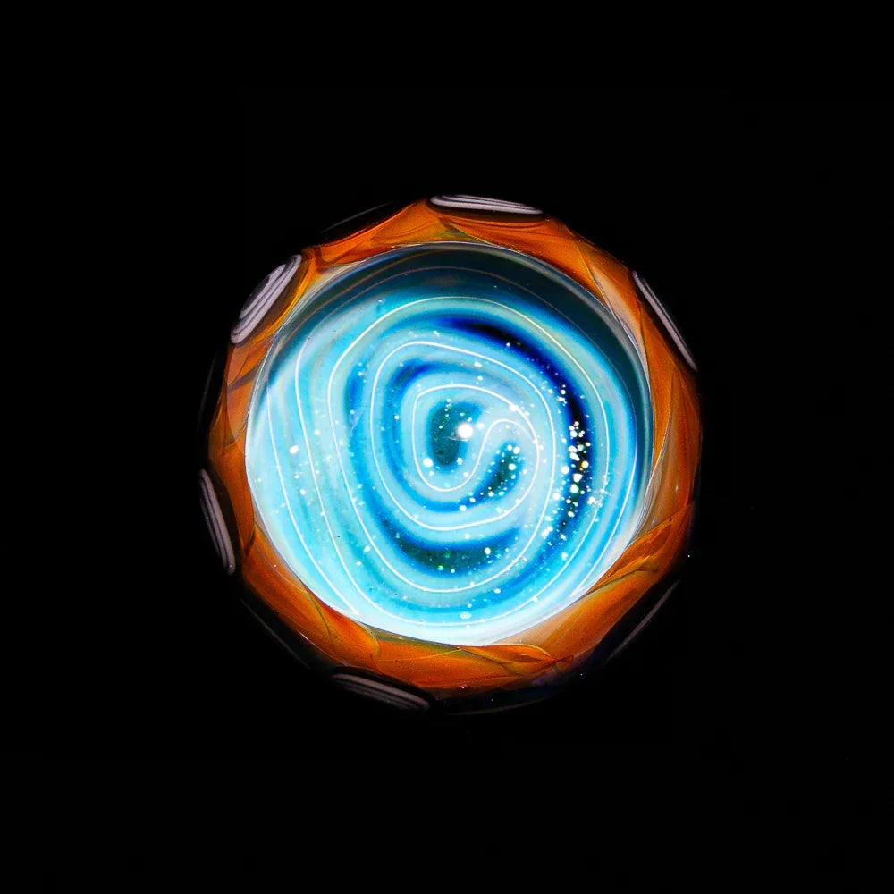 Handmade glass marble with blue spiral vortex and silver fume accents against black background