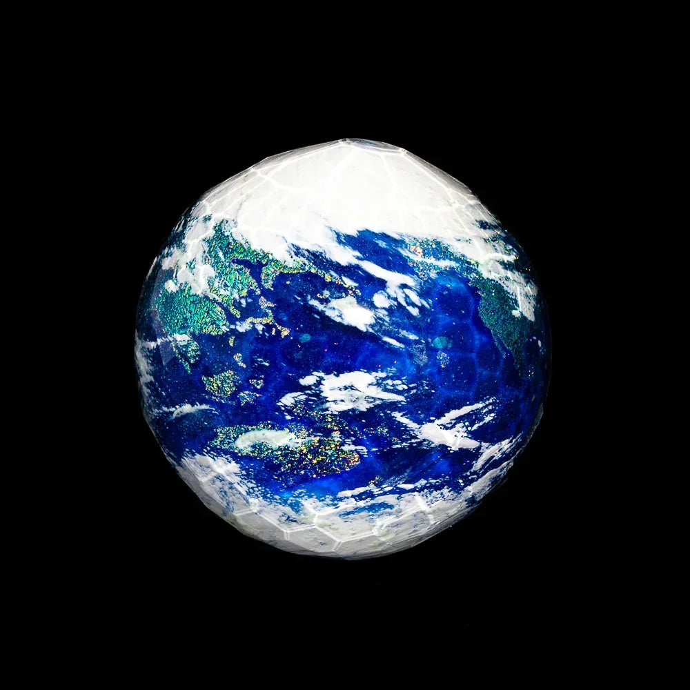 Faceted glass marble with blue, green, and white earth-like design on black background