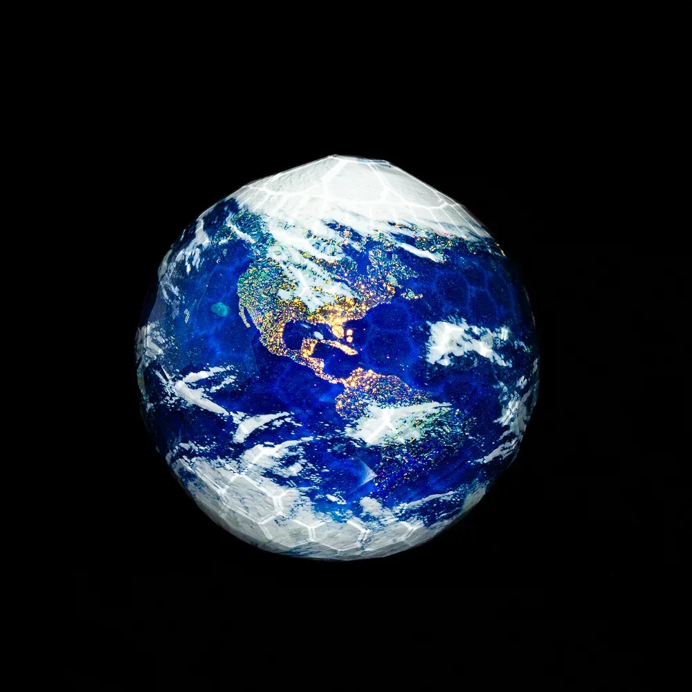 Faceted glass marble resembling Earth with blue, white, and iridescent details on black background