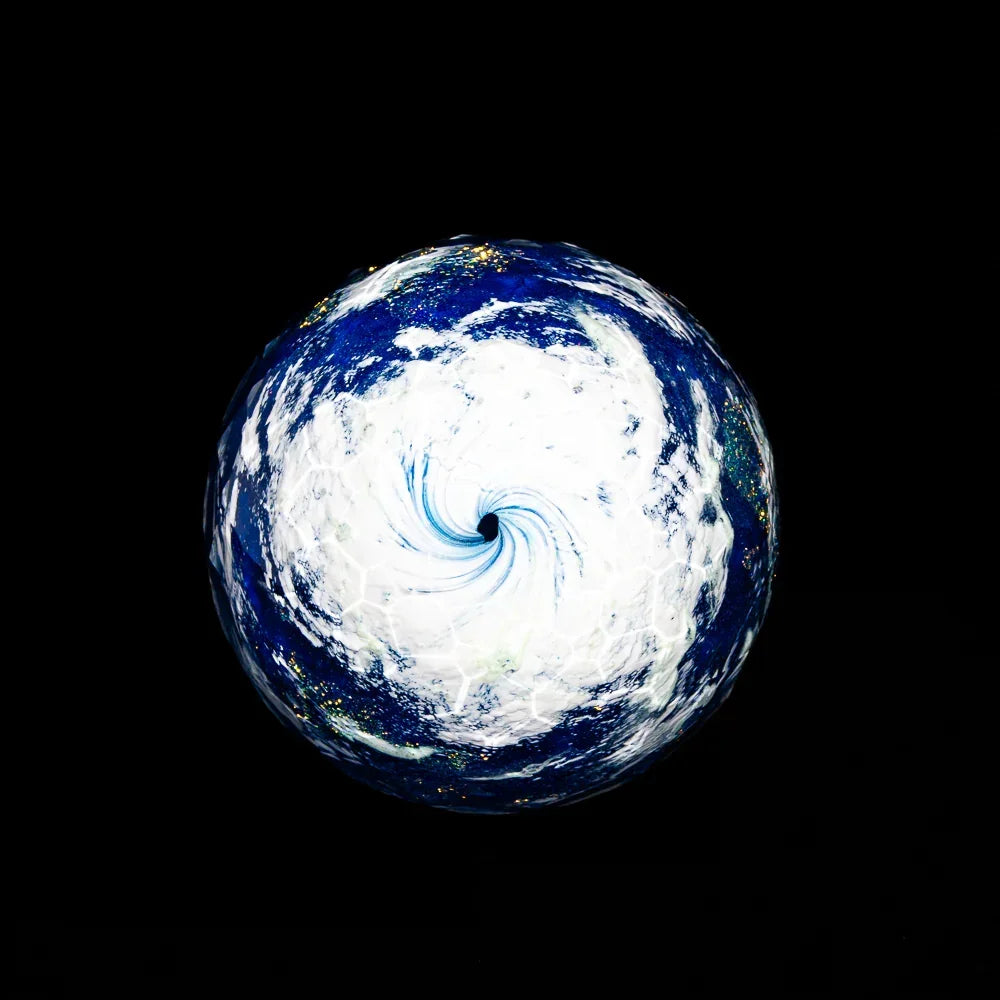 Faceted glass marble with swirling blue and white earth design on black background