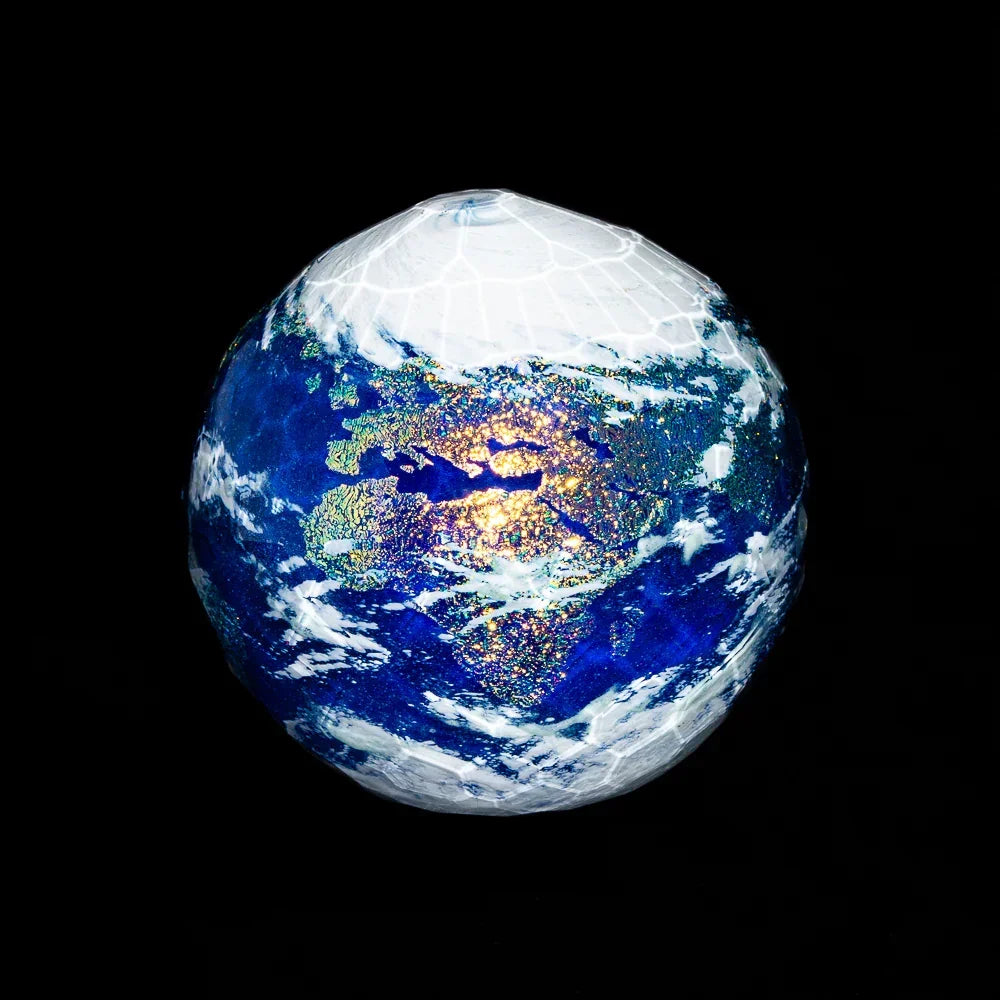 Faceted glass marble resembling Earth with blue, white, and iridescent details on black background