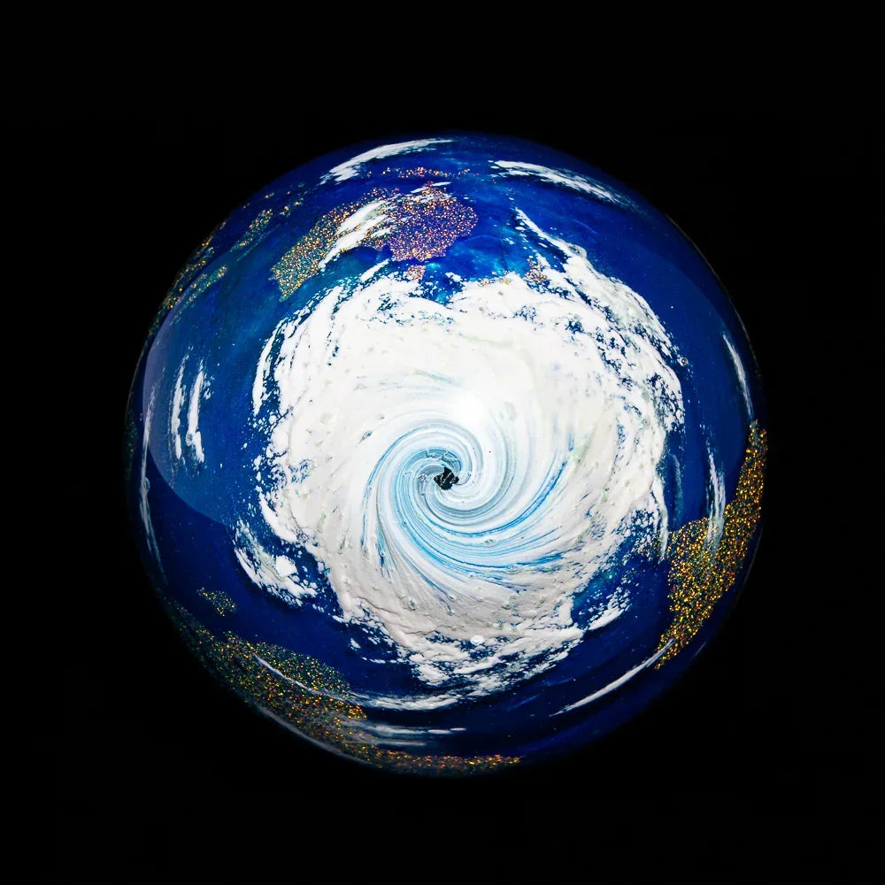 Handcrafted glass marble with swirling blue, white, and gold Earth design on black background.