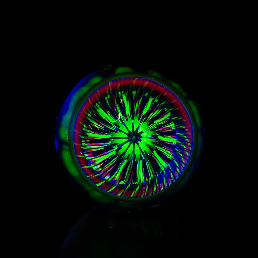 Handcrafted glass marble with vibrant UV-reactive green and blue geometric patterns