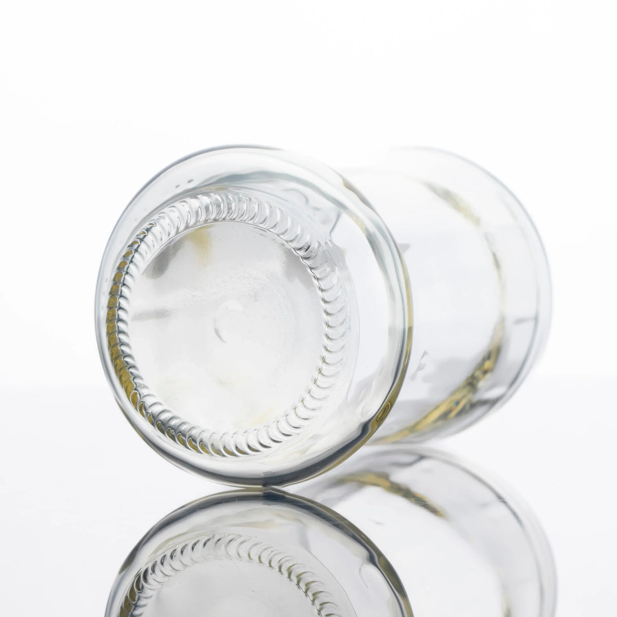 Clear glass cup shaped like a classic soda bottle, shown on a white reflective surface