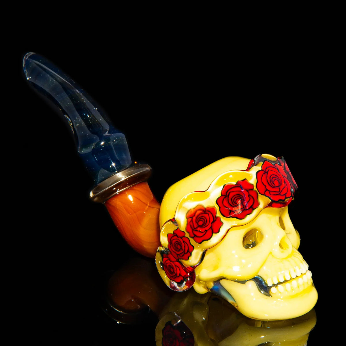 Glass pipe shaped like a yellow skull with red rose crown and blue mouthpiece