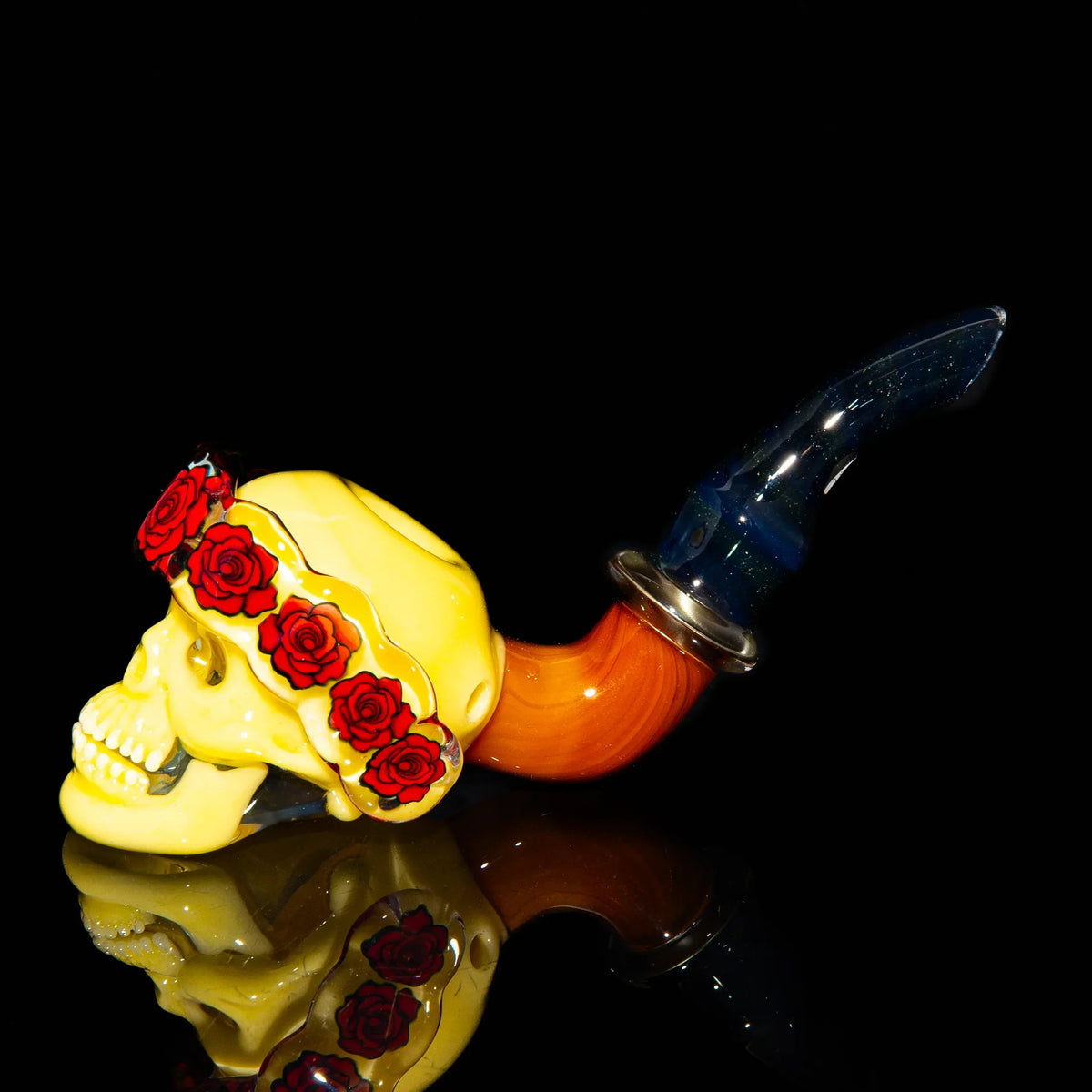 Hand-blown glass pipe shaped like a yellow skull with red roses, curved blue and orange stem