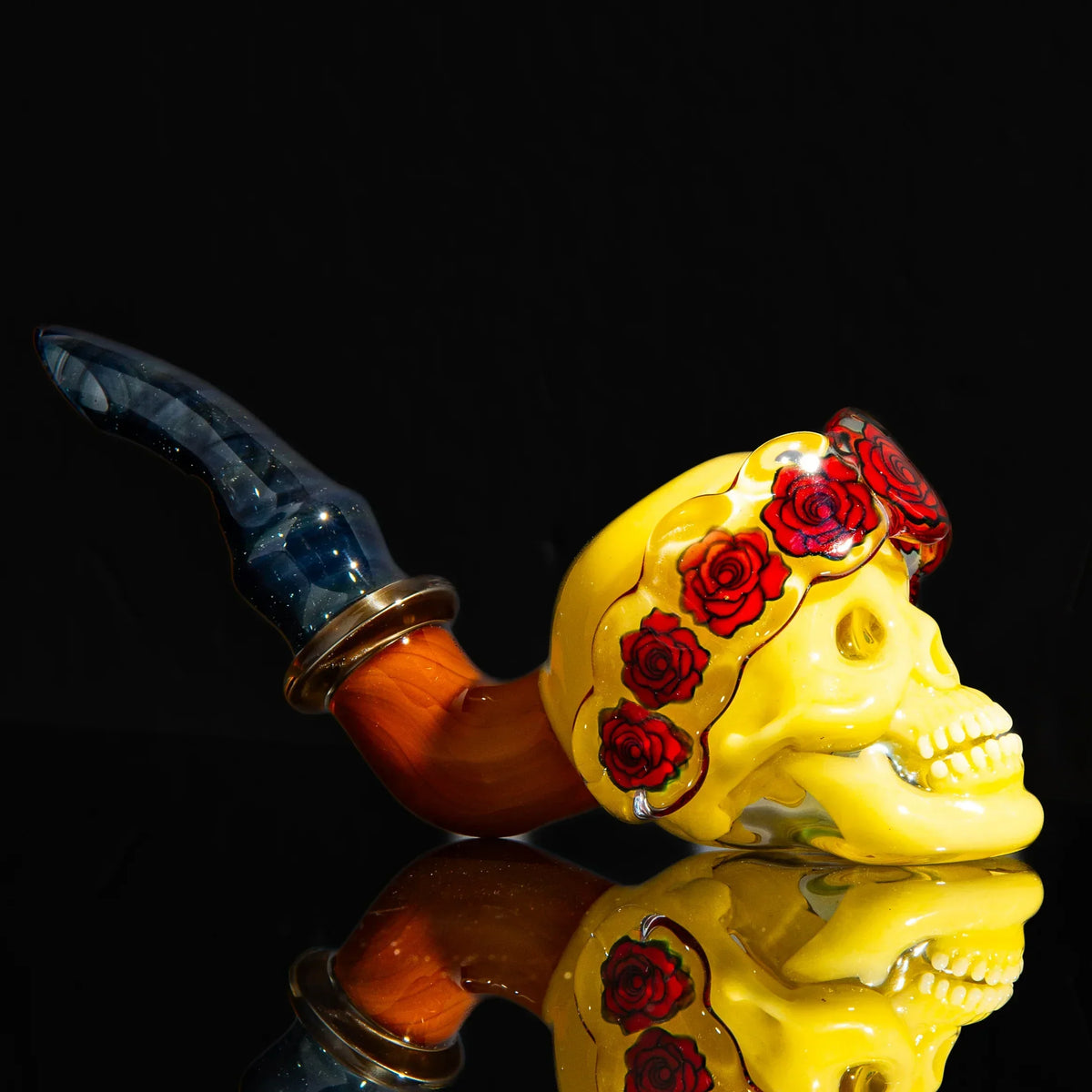 Handcrafted glass pipe shaped as a yellow skull with red roses and a blue marbled stem