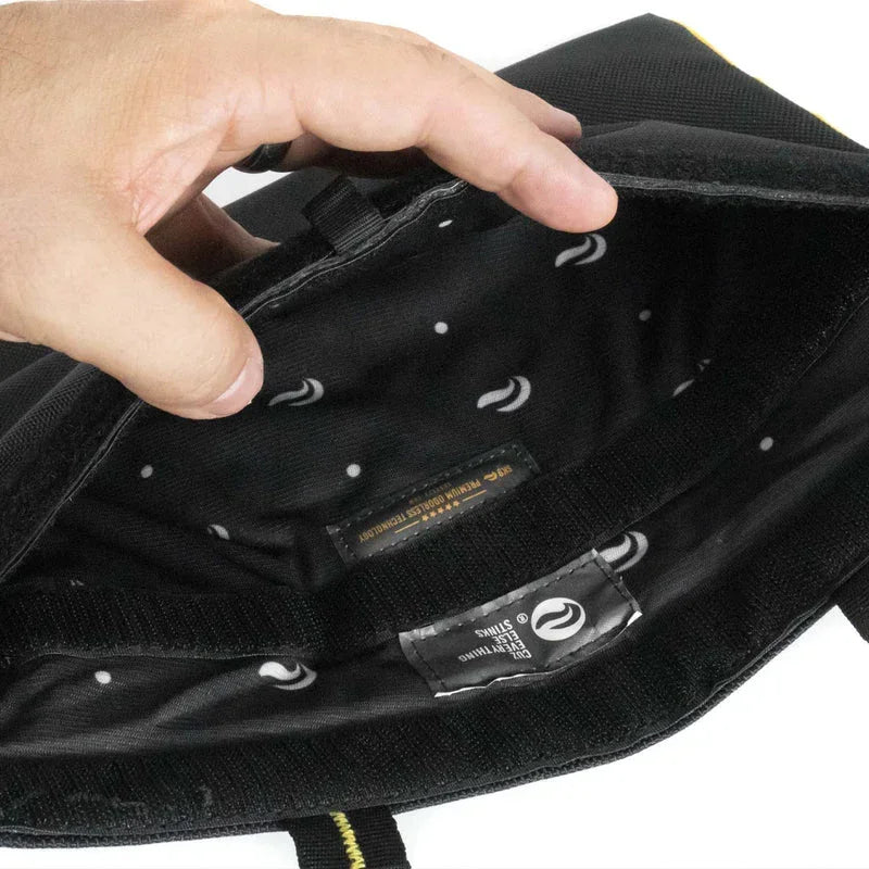 Hand holding open a black bag with patterned interior and stitched labels visible inside.