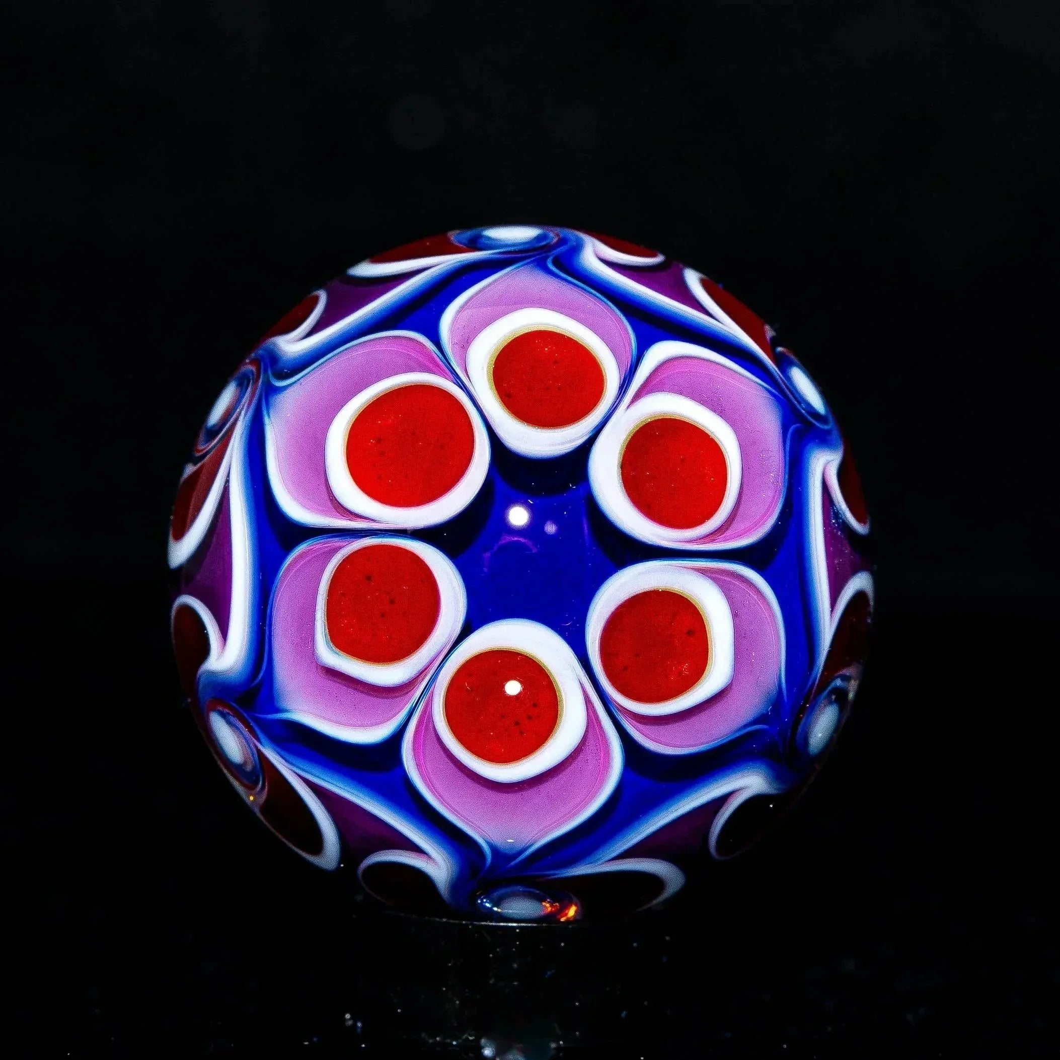 Colorful glass marble with intricate red, white, and purple dot patterns on blue background.