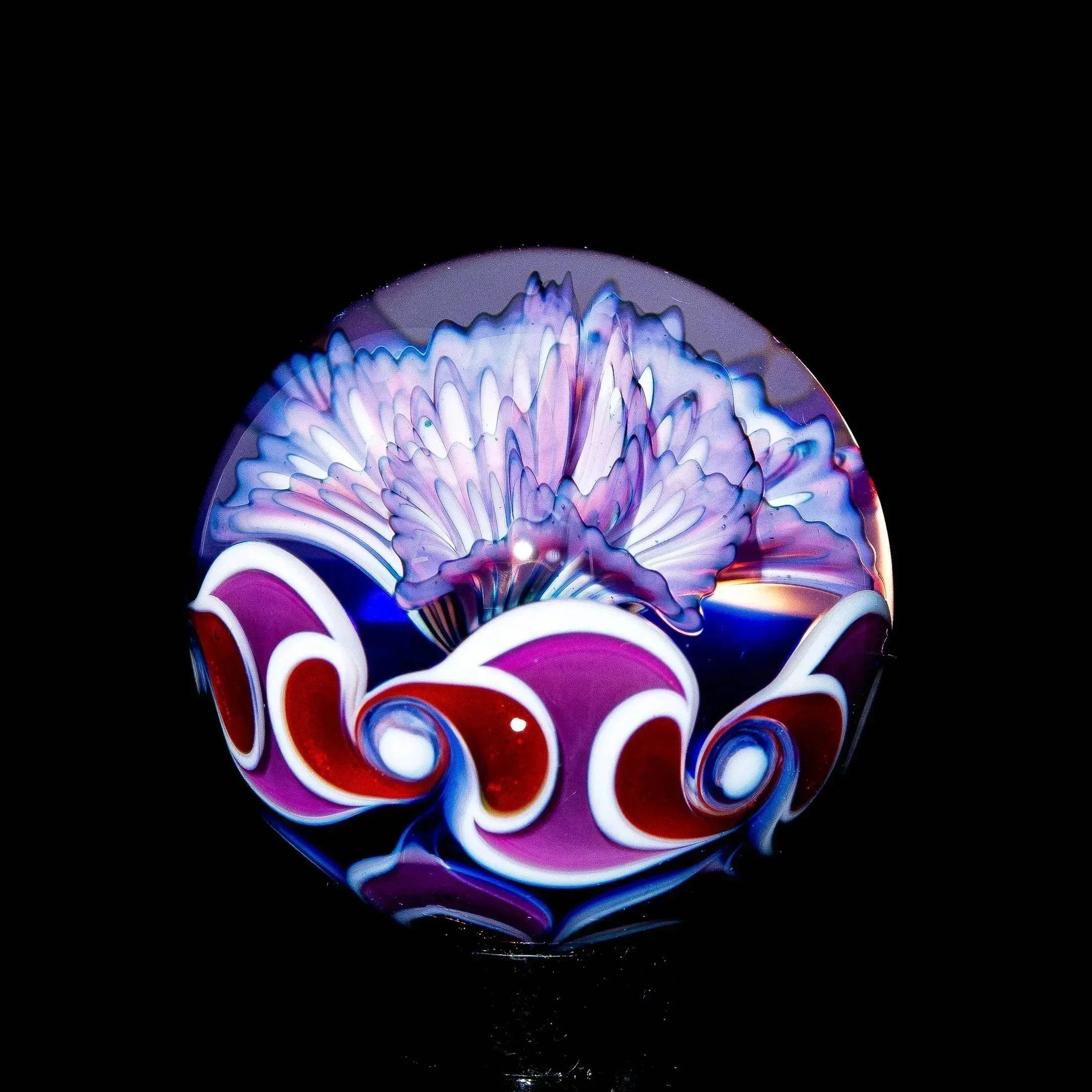 Hand-blown glass marble with purple flower and swirling red and white accents on black background