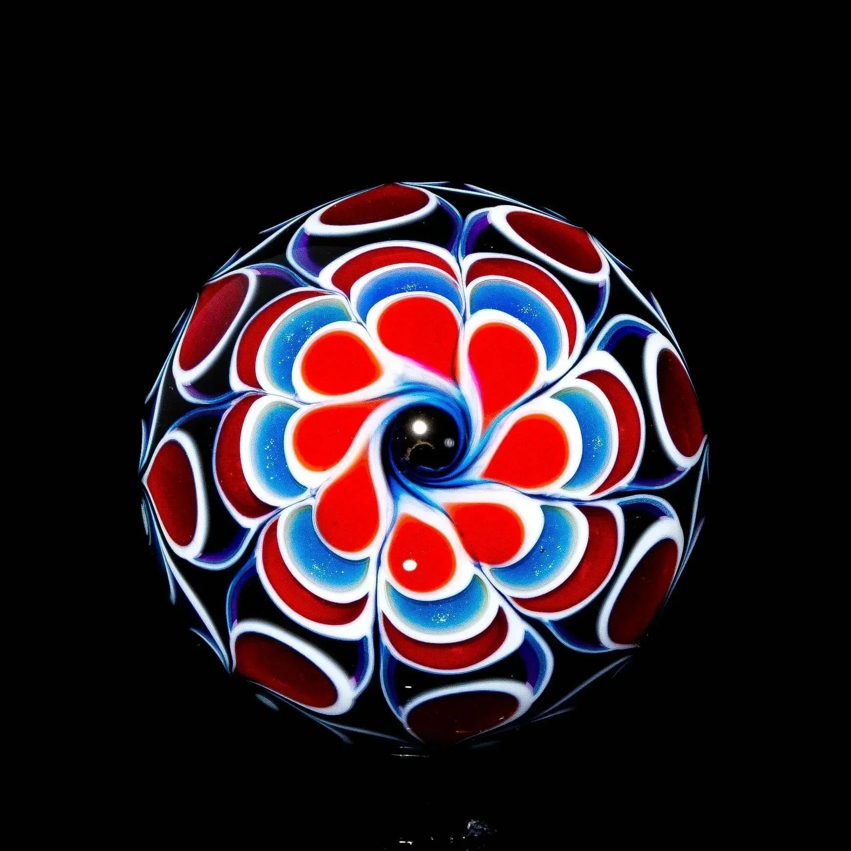 Handcrafted glass marble with red, white, and blue wig wag swirl pattern on black background