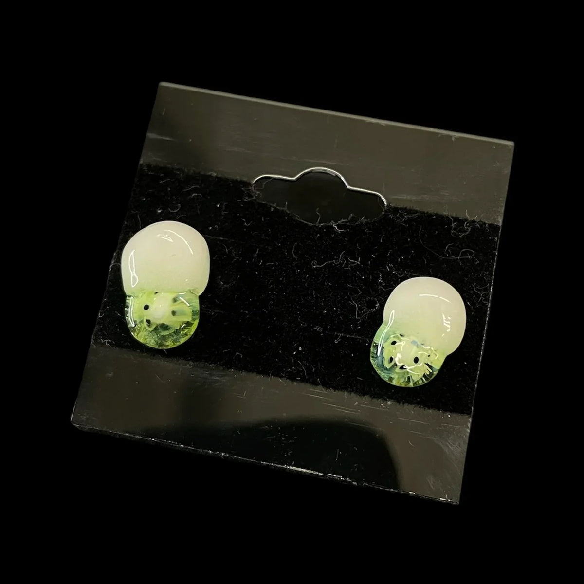 Glass kiwi fruit earrings with white tops on a black display card