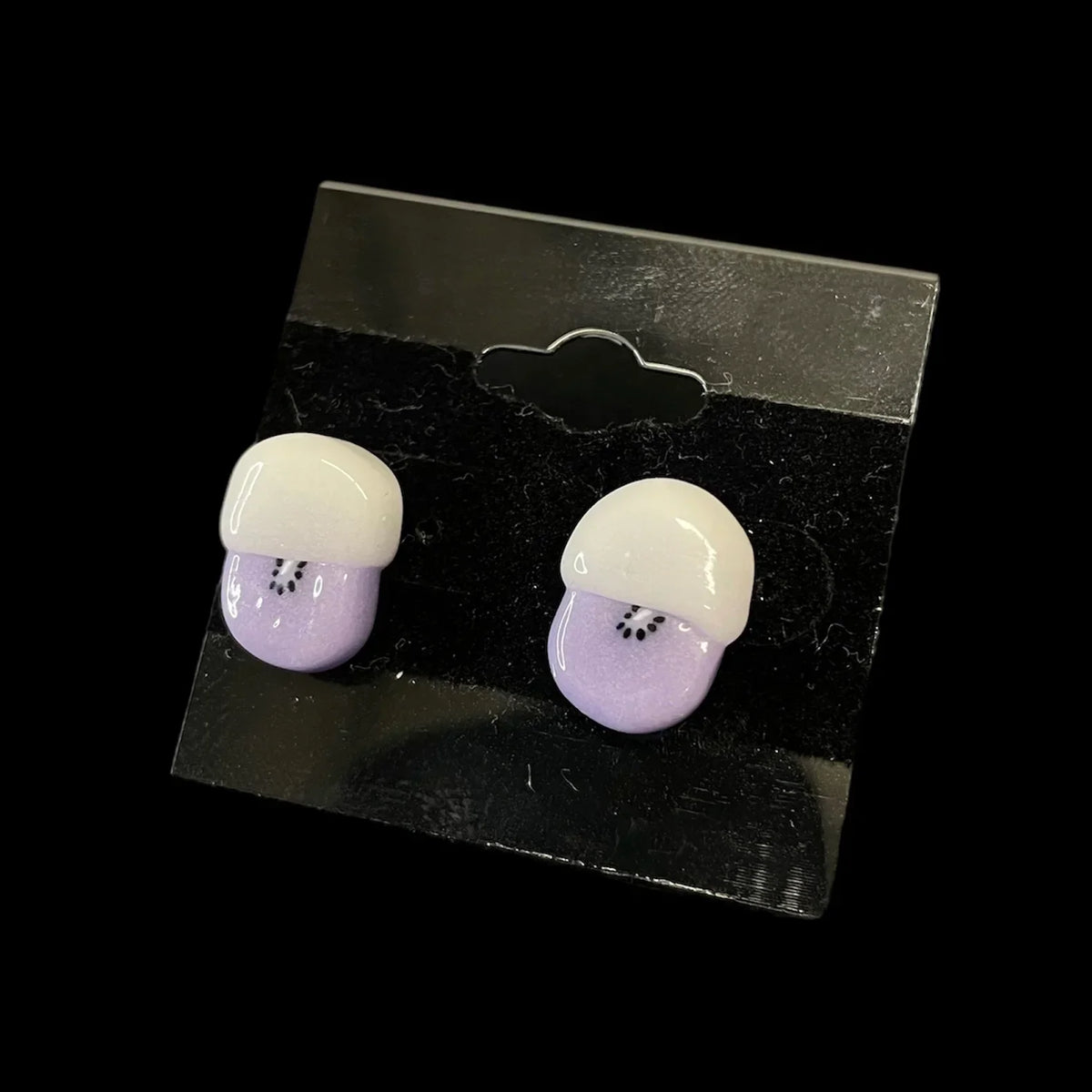 Pair of handmade glass kiwi stud earrings with white tops and purple bases on display card