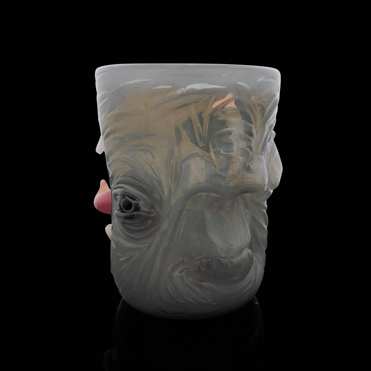 Pastel glass mug with sculpted abstract face, unique art glass drinkware on black background.